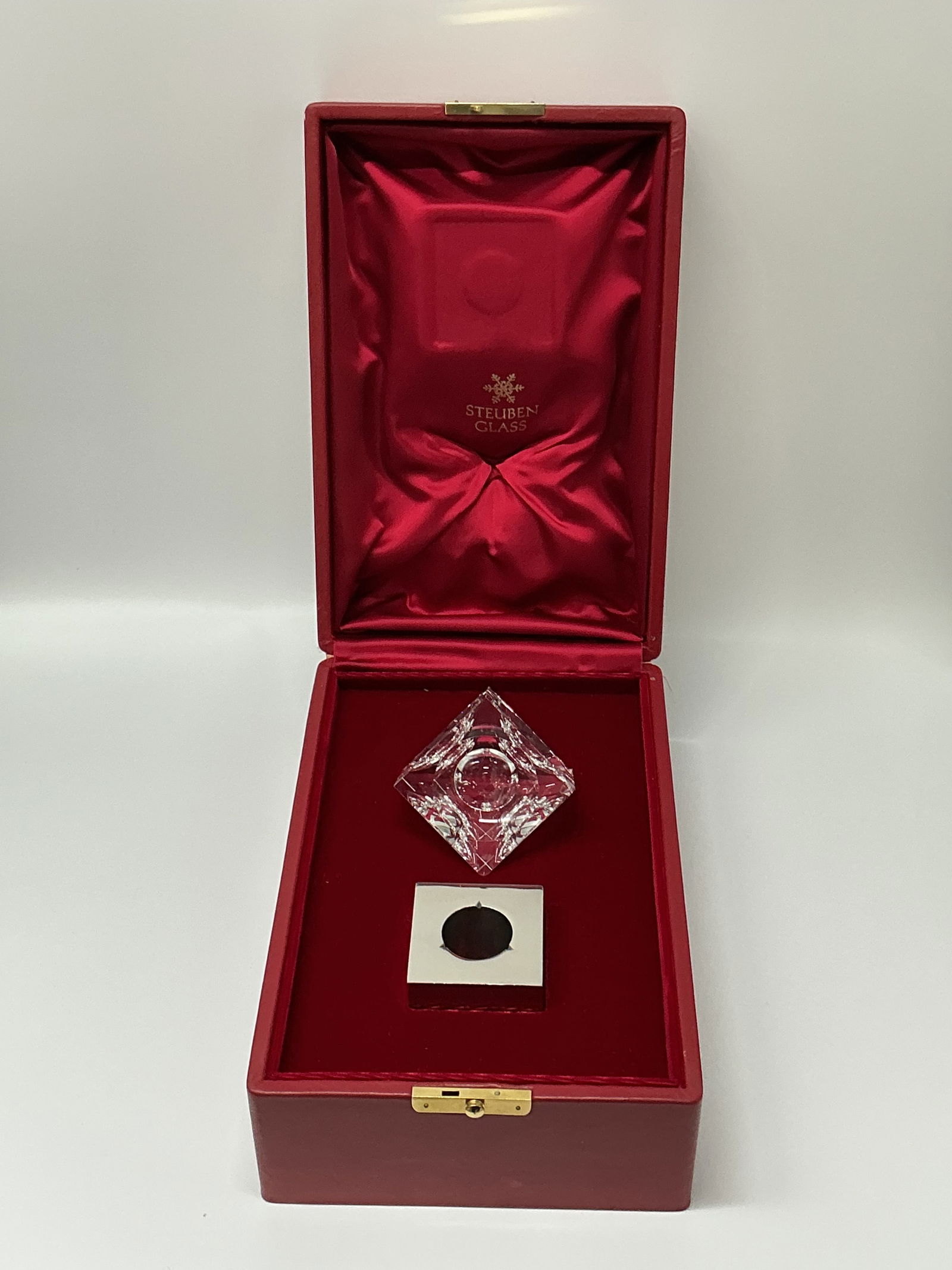Steuben Glass Cube with Metal Stand in Presentation Box: Steuben glass cube with a geometric design, accompanied by a metal stand. Presented in a fitted red presentation box with satin lining. Cube and stand measures approximately 2.5 inches each in length,