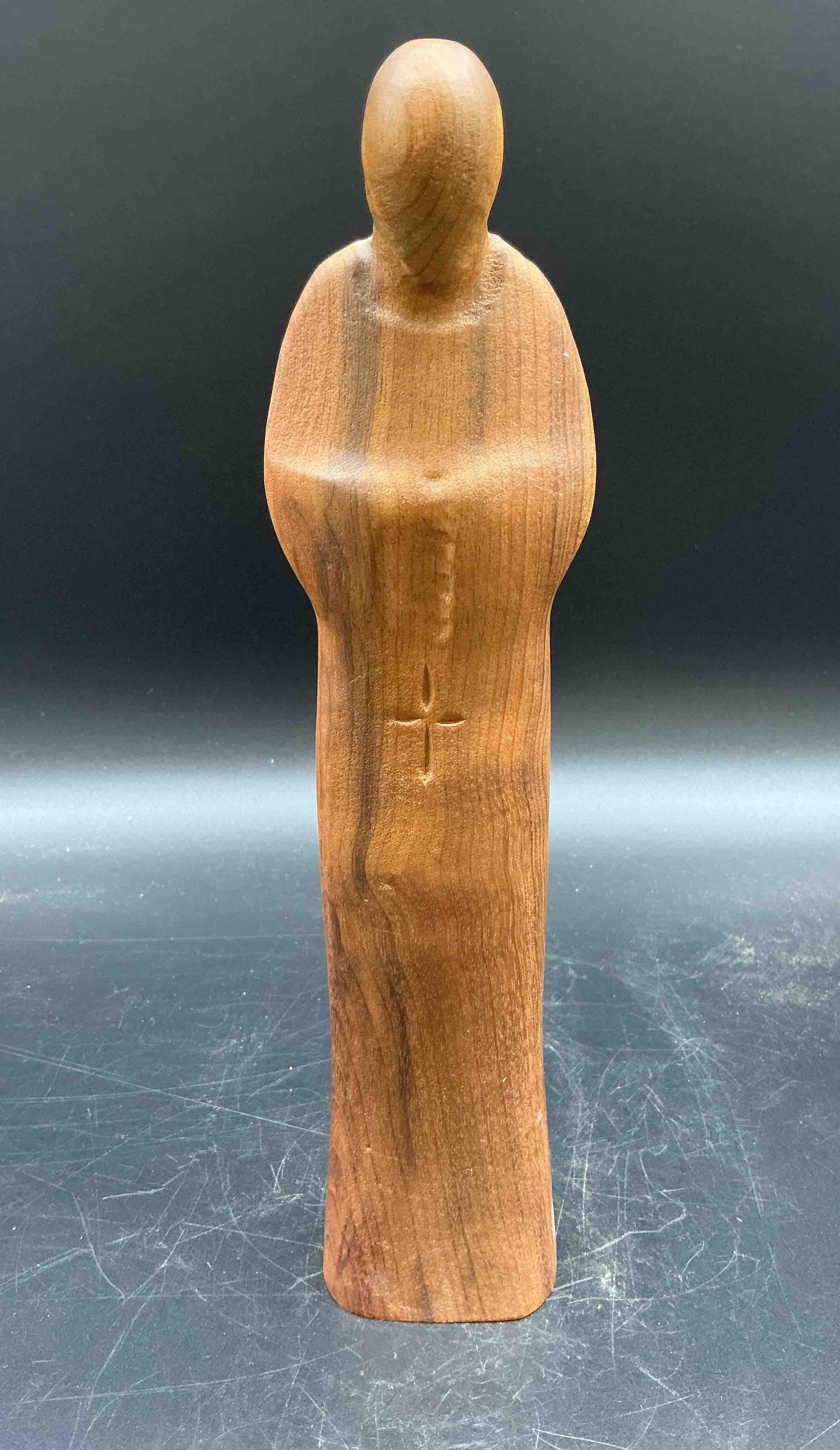 Minimalist Wooden Figure in Prayer: Smooth, abstract wooden sculpture of a standing figure with bowed head and hands together in a prayer or meditative pose. The simplified form emphasizes serenity and spiritual introspection. Medium: H
