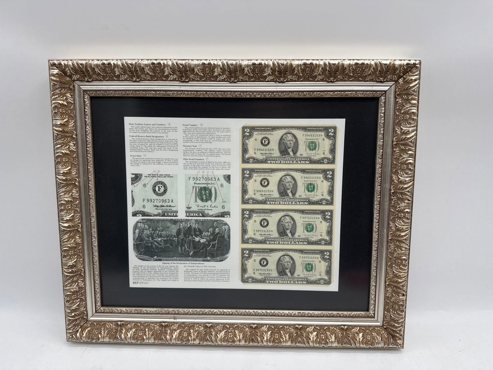 Framed Bicentennial (1976) History of the Two Dollar Bill with Uncut Sequence of same: Framed display featuring a Series 1976 $2 bill along with informational text about the bill's design and features. The bill and text are mounted on a black background within a decorative silver-to