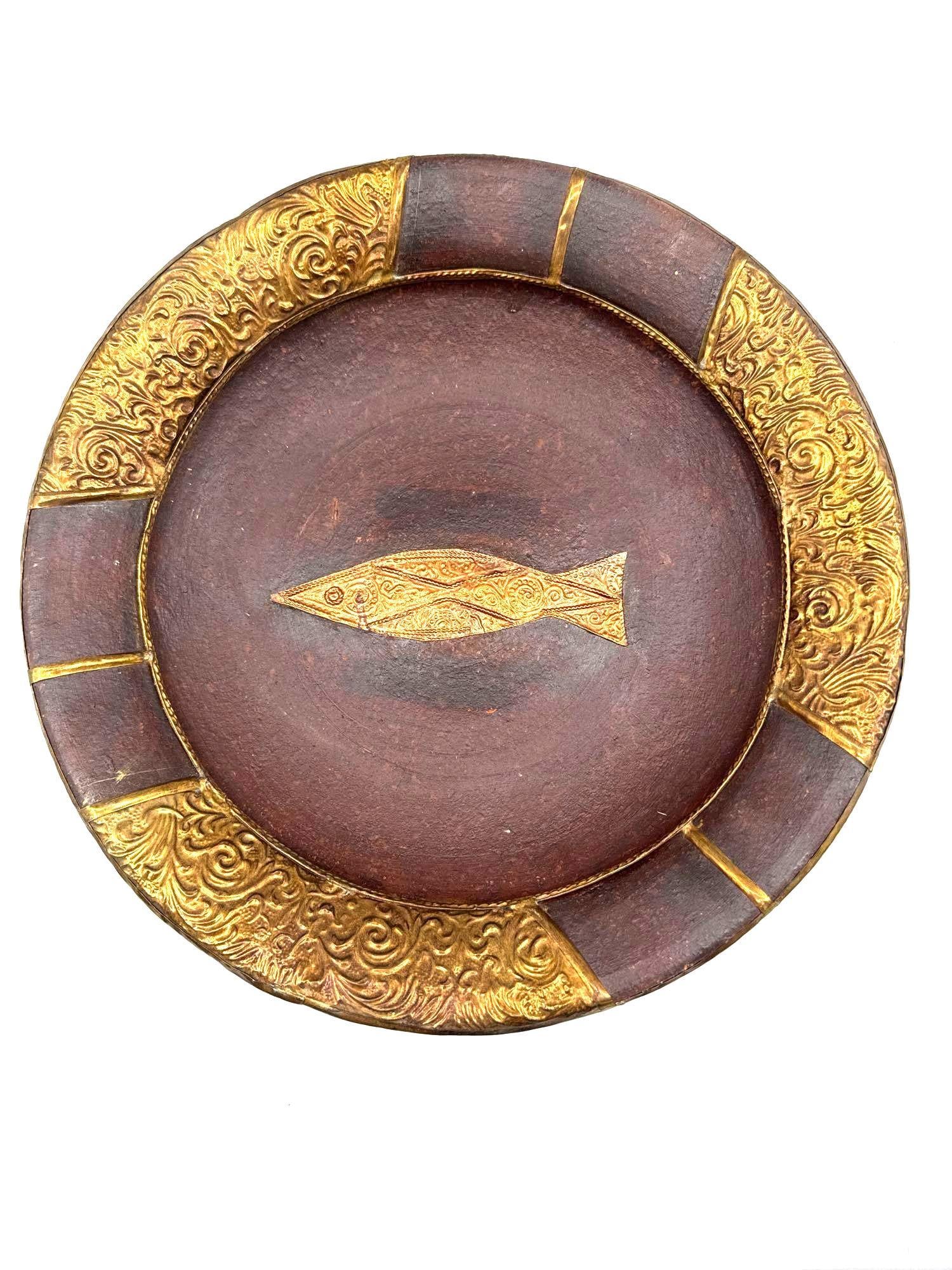 Decorative Fish Motif Plate: Round brown plate featuring a central embossed fish design and alternating gold floral relief panels along the rim. Likely intended for display.Medium: Hand-painted and embossed resin or composite mat
