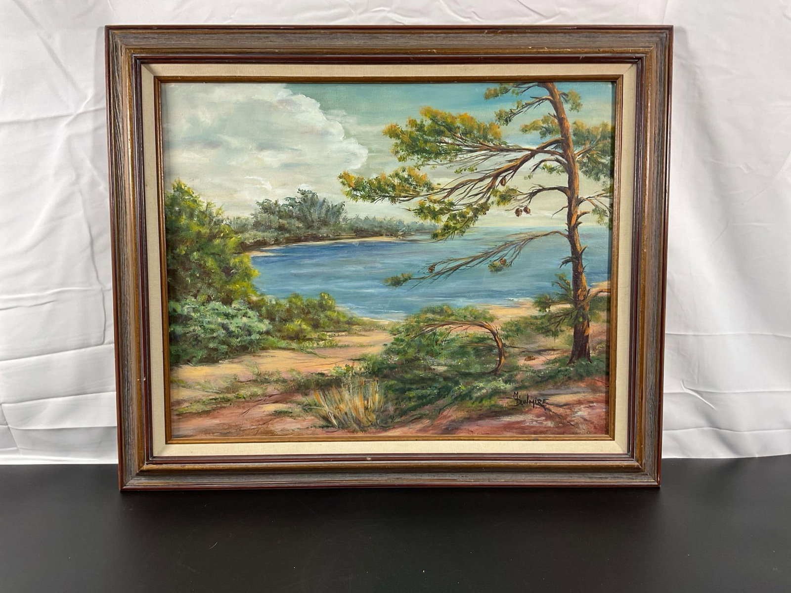 Lakeside Serenity by Marianna Dunmire (American) Oil on canvas: This tranquil landscape painting by Florida artist Marianna Dunmire depicts a peaceful lakeside scene with a gently curving shoreline, a vibrant mix of greenery, and a prominent pine tree in the 