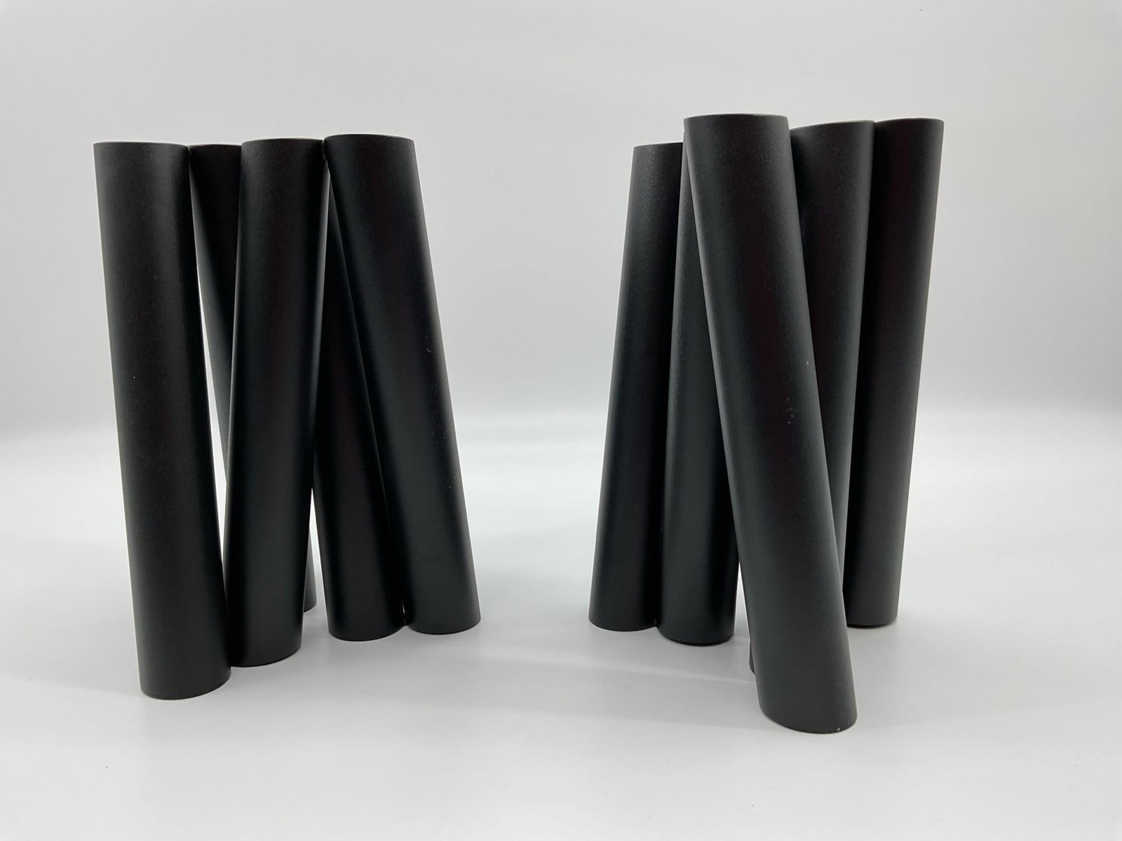 Set of Black Tubes Sculpture: This abstract sculptural arrangement consists of a set of matte black cylindrical tubes, grouped into two separate clusters. Each tube tapers slightly and is arranged vertically, resembling minimalist