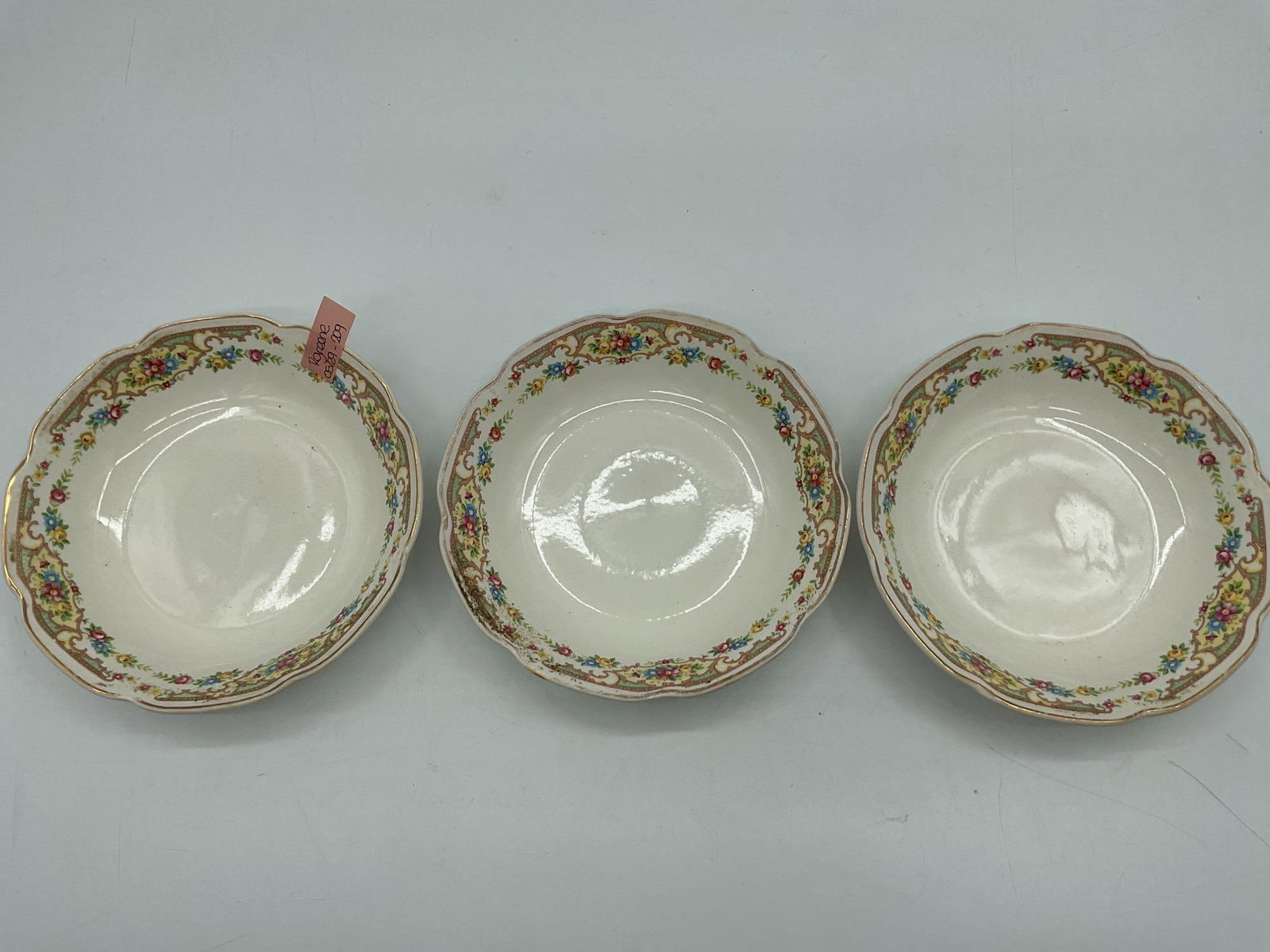 Set of Floral Rimmed Scalloped Bowls with Gold Trim: Trio of ivory-toned porcelain bowls featuring scalloped edges, gold trim, and a continuous floral garland border in pink, blue, and yellow. Likely American or European mid-century china. Dimensions: H