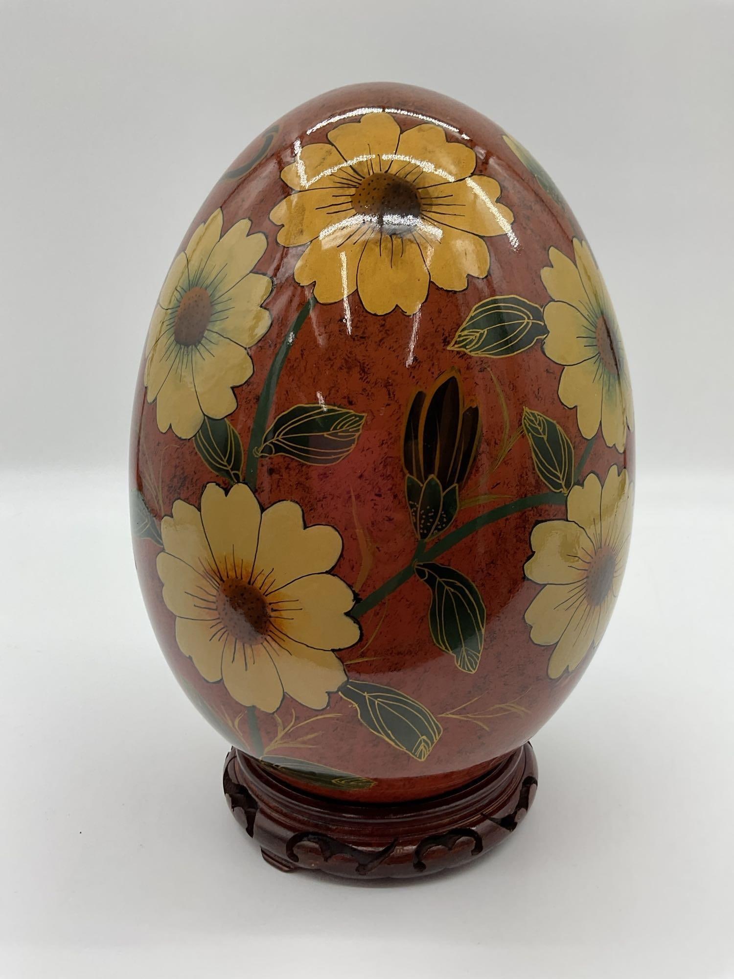 Hand-painted Floral Decorative Egg: Large egg-shaped ceramic decorative piece with a warm marbled terracotta glaze, hand-painted with yellow and brown flowers and green leaves. Finished with a glossy coat and displayed on a carved woode