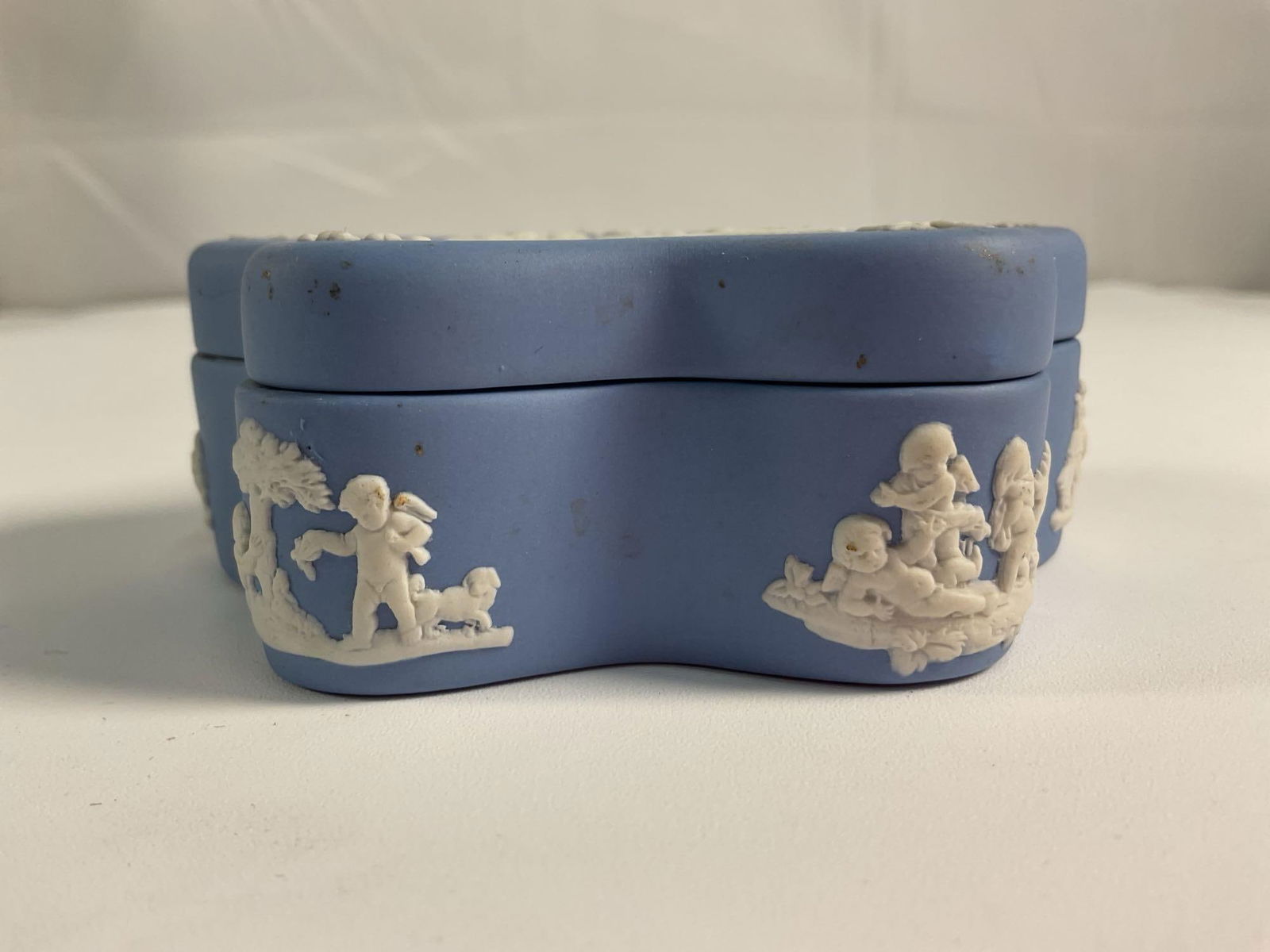 Wedgwood Jasperware Lidded Trinket Box: A charming Wedgwood Jasperware lidded trinket box in soft blue with a unique floral-shaped design. The lid features intricate white bas-relief depicting classical figures surrounded by delicate floral