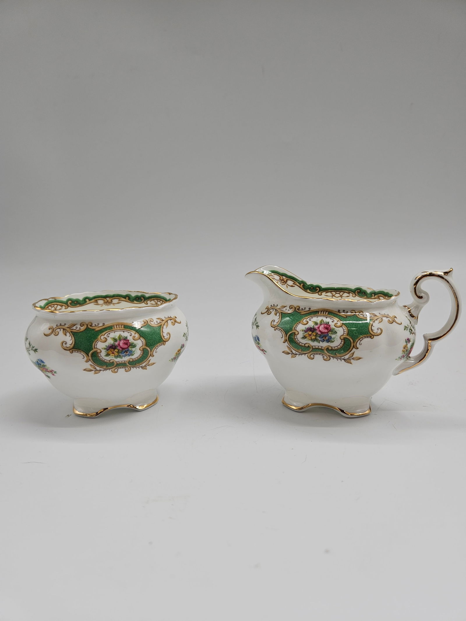 Coalport Green and Gold Floral Creamer and Sugar Set: Elegant Coalport porcelain creamer and sugar bowl set featuring ornate hand-painted floral medallions framed by emerald green panels and lavish gold gilt detailing. Both pieces display the refined cur