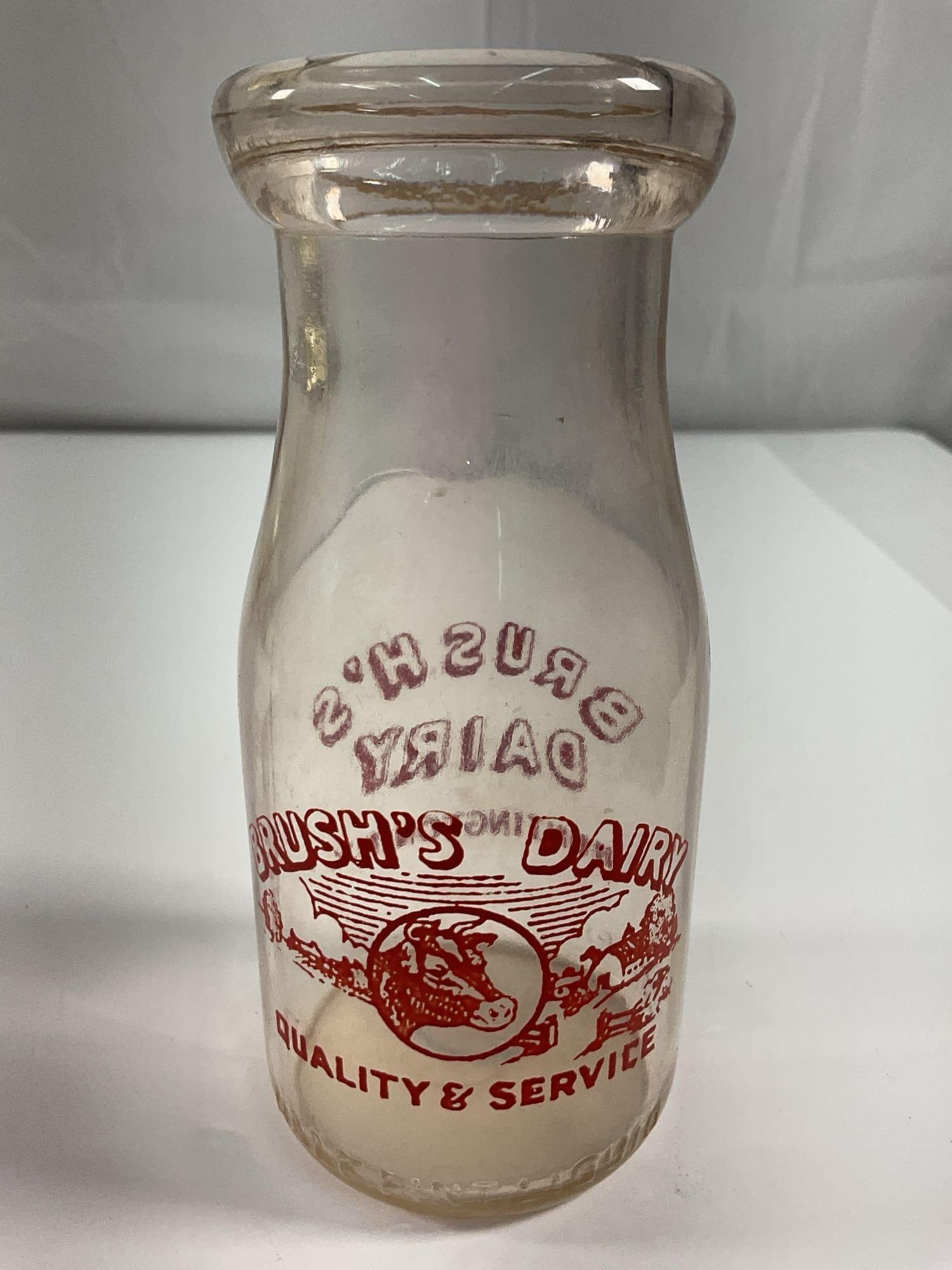 Brush’s Dairy Cream Bottle - Box 5 - Photo 13:  A small, clear glass dairy bottle from Brush’s Dairy, featuring red printed lettering and an illustration of a cow. The text highlights "Quality & Service," a common marketin