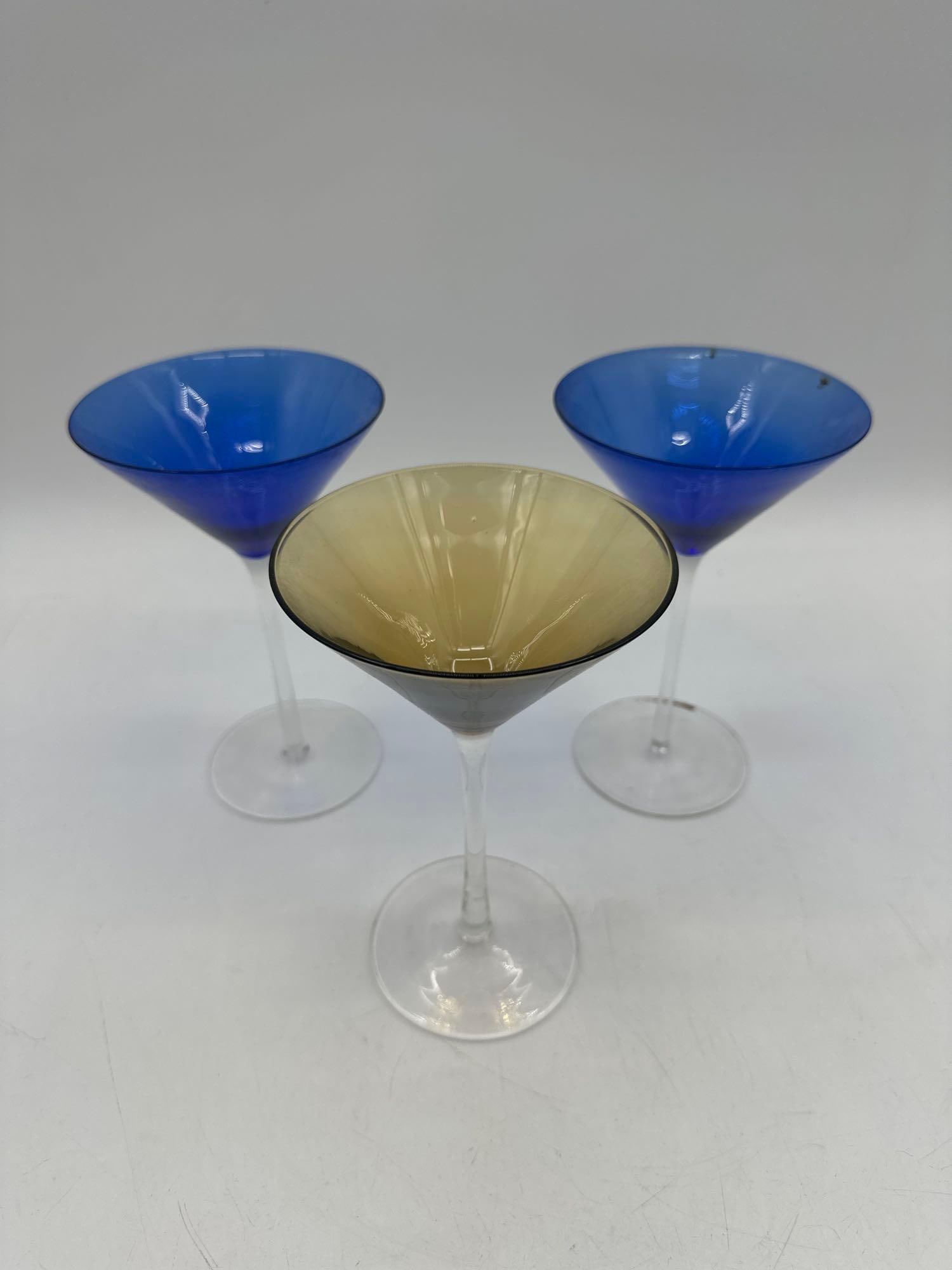 Set of Three Colored Stemmed Glasses: Set includes two cobalt blue and one amber-colored conical martini-style glasses on clear stems. Medium: Colored glass Dimensions: H7.5in x L5in x W5in