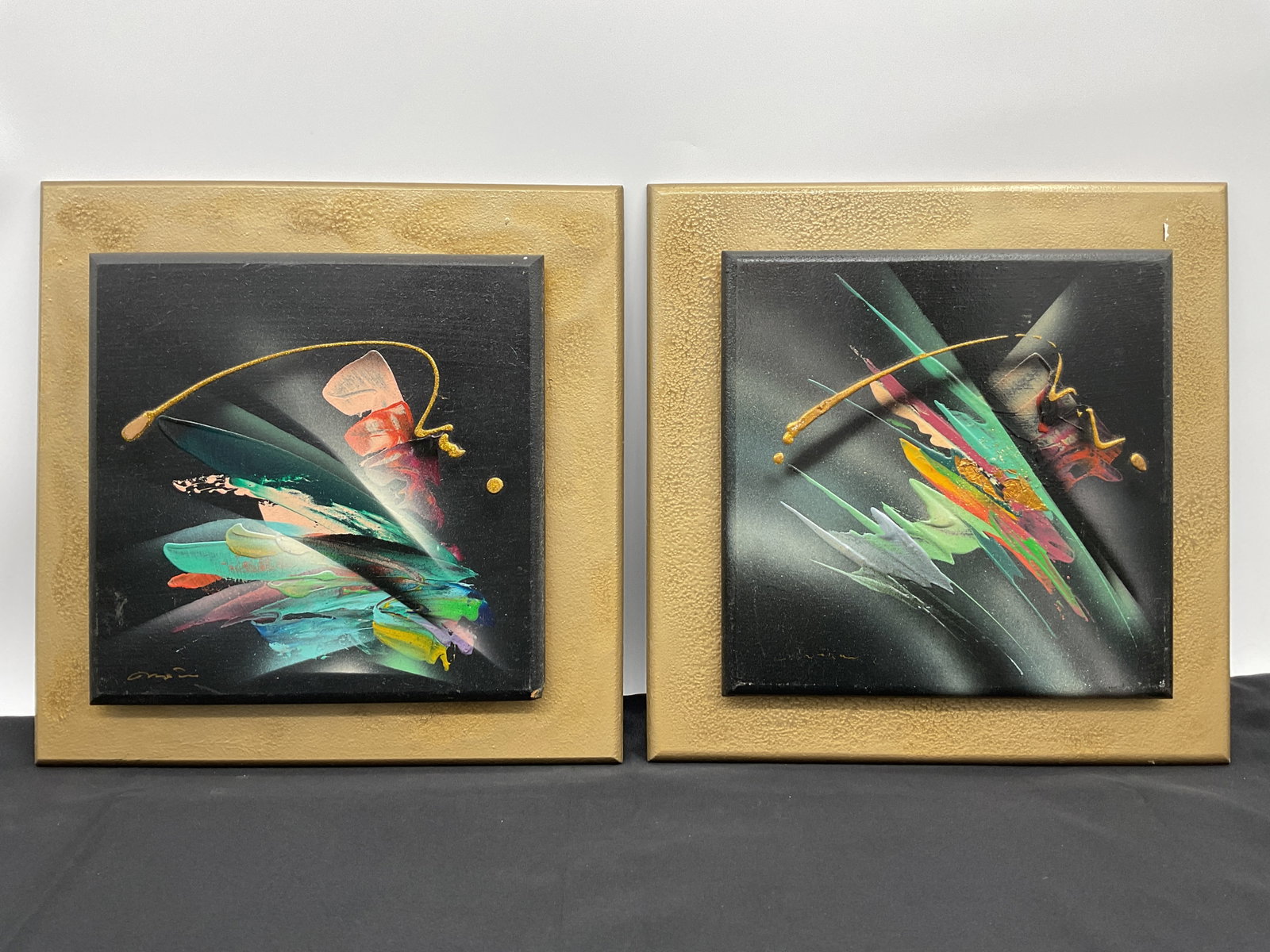 Pair of Abstract Paintings on Canvas, Framed: A pair of decorative abstract paintings on canvas, each framed. The paintings feature colorful, dynamic compositions against a dark background. Each measures 16 x 16 inches.