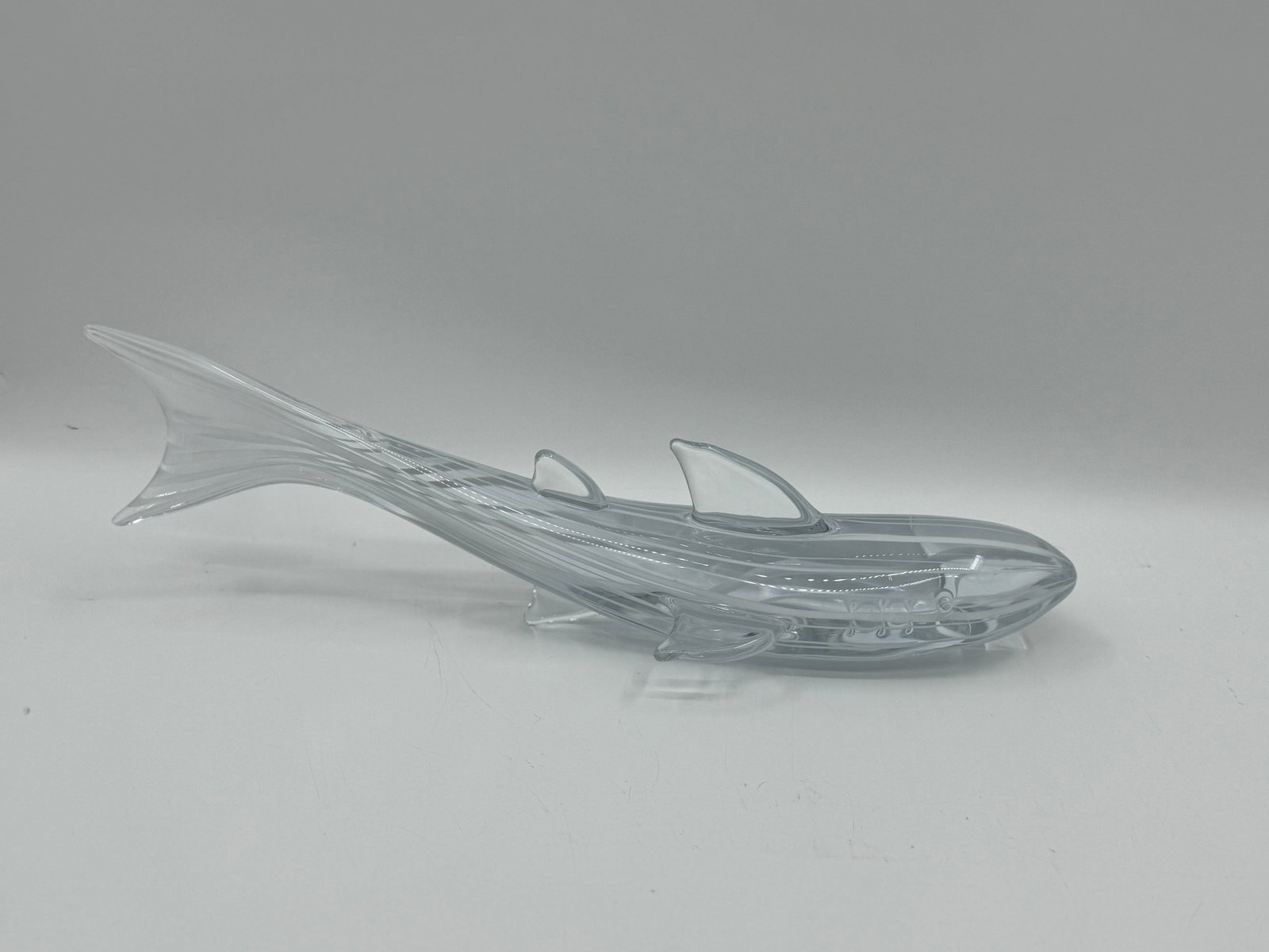 Clear Glass Shark Sculpture, 21 inches: Clear glass sculpture depicting a shark. The piece measures approximately 21 inches in length, 5 inches in height, and 6 inches in width. A decorative piece suitable for display.