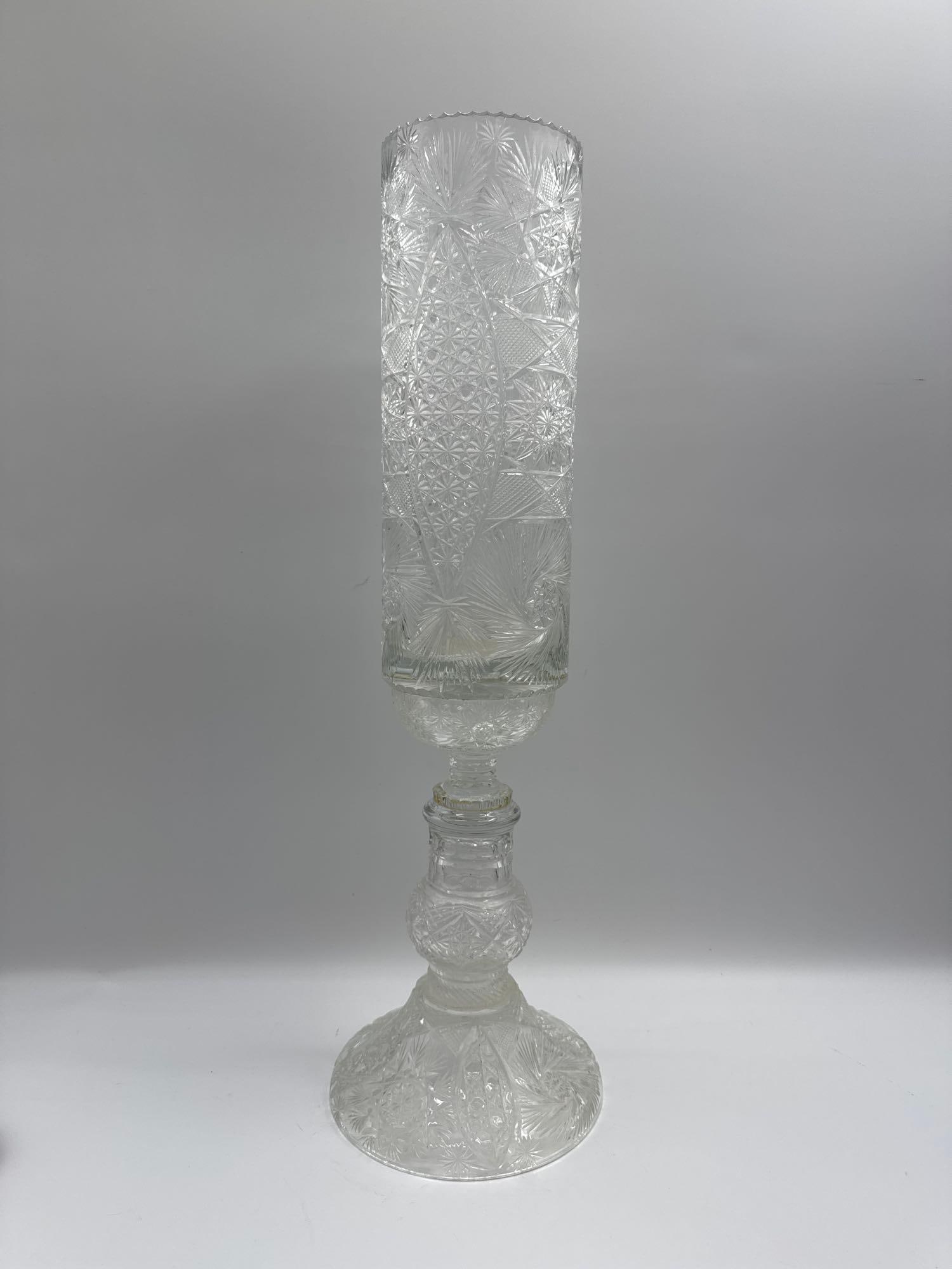 Tall Cut Glass Vase on Pedestal Base: Elegant tall cut glass vase with intricate starburst and geometric patterns. The piece features a cylindrical body raised on a bulbous pedestal stem and wide circular foot, all richly decorated with d