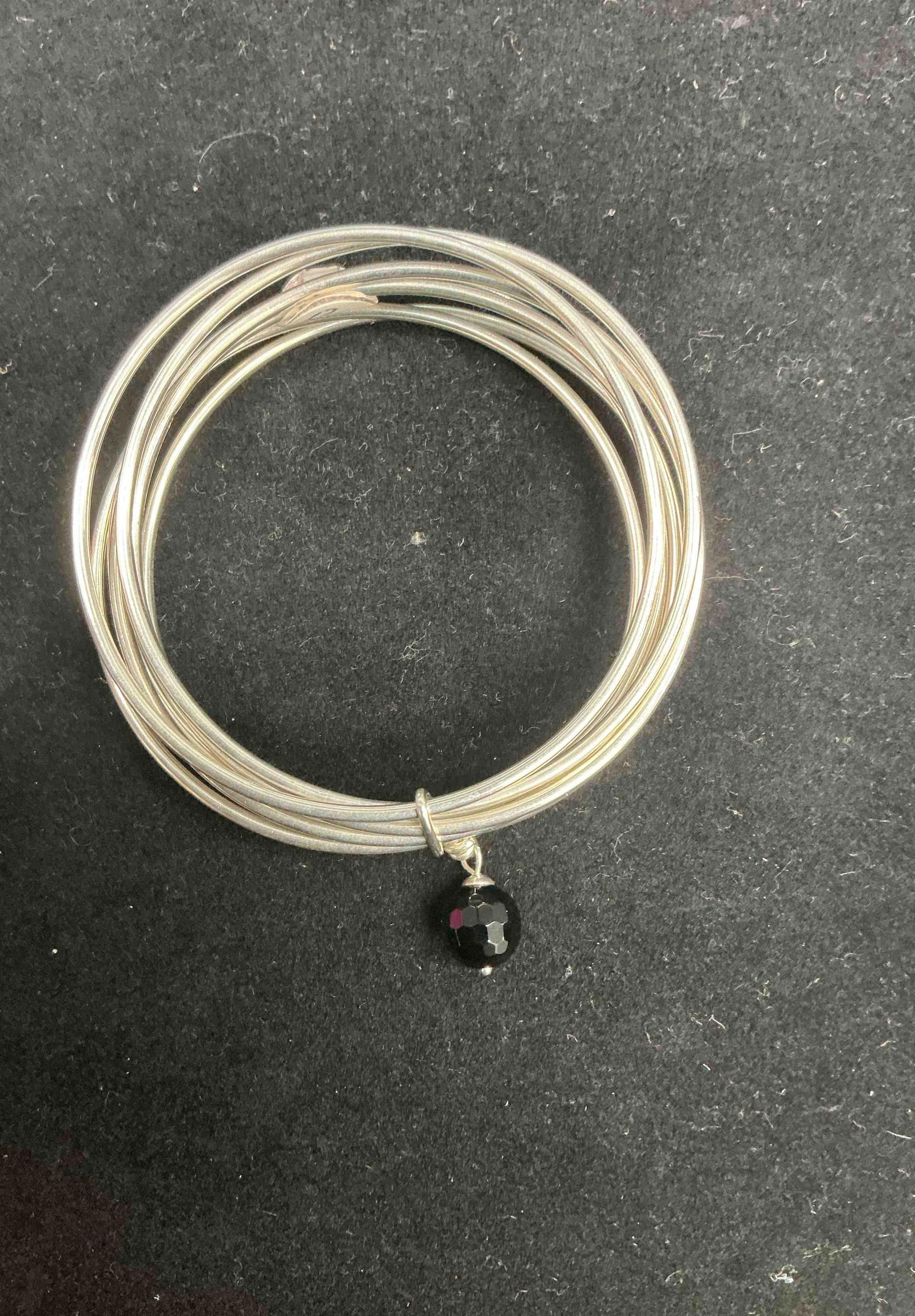 Set of Seven Sterling Silver 925 Bangle Bracelets with Dangling Black Bead, Size 7.5 – 26.13g: Elegant set of seven sterling silver bangles, stamped 925, with a combined weight of 26.13 grams. Crafted in a polished finish, the set is accented by a single faceted black bead charm that adds a tou