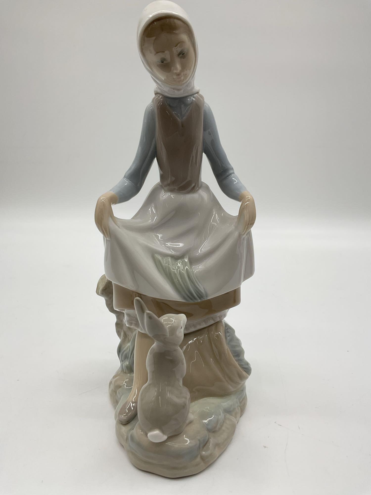 Lladro Girl with Rabbit and Lamb Figurine - 4826: A glazed porcelain sculpture of a young girl in a headscarf gently holding her skirt, with a rabbit and lamb at her feet in a pastoral scene. Dimensions: H9in L4in W4in Medium: Glazed porcelain