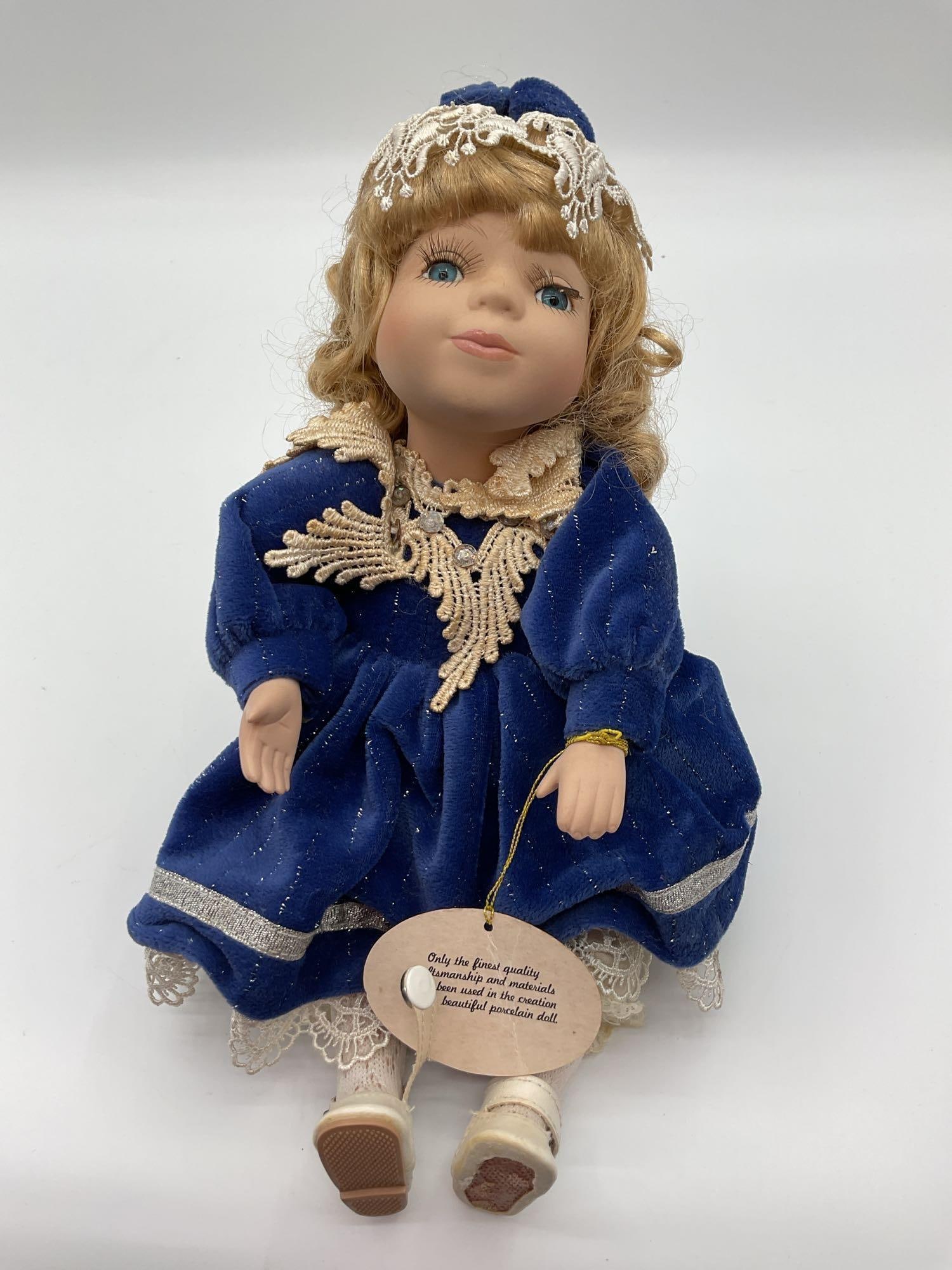 Collectible DanDee Musical Genuine Fine Bisque Porcelain Doll: This collectible porcelain doll is elegantly dressed in a royal blue gown with lace detailing and shimmering fabric accents. She has long curly blonde hair, striking blue eyes, delicately painted faci