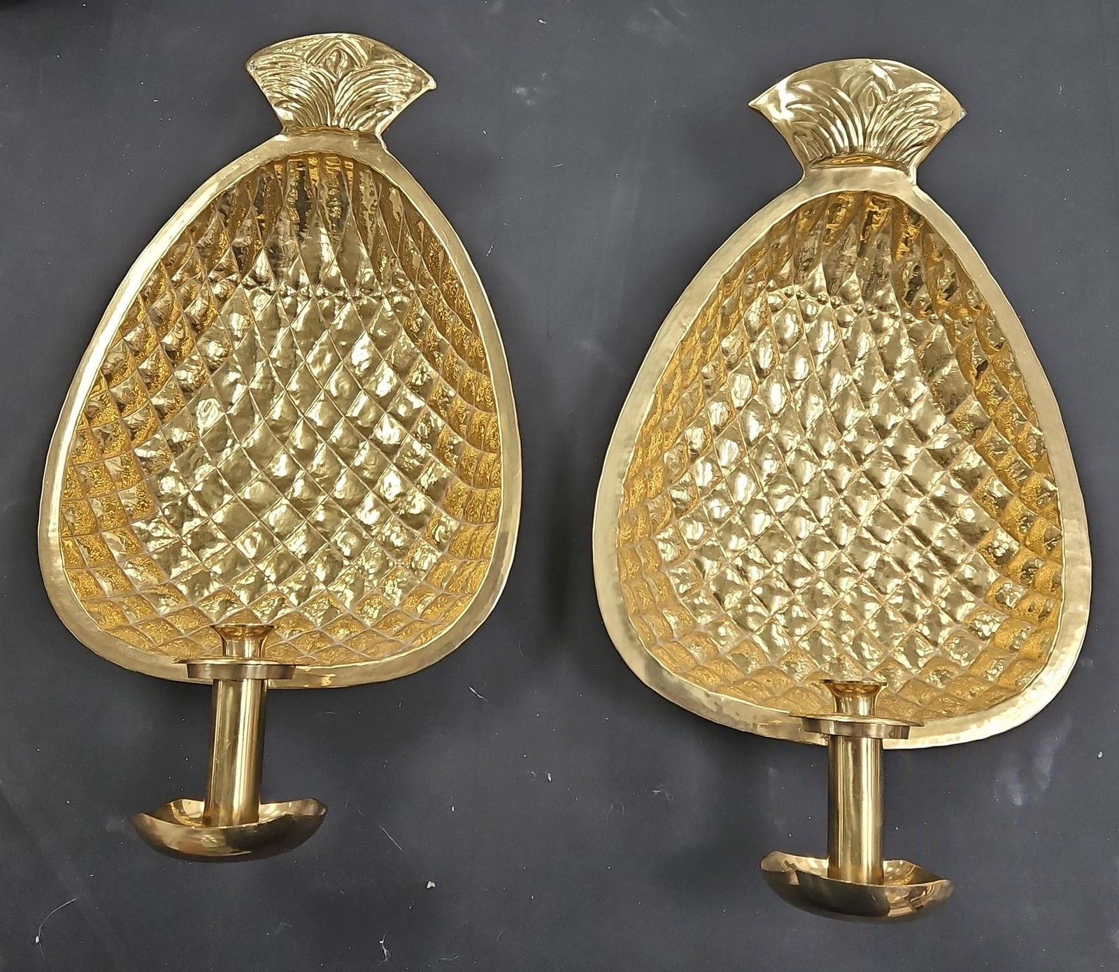 Pair of Brass Pineapple Wall Sconces: A matching set of brass wall sconces designed in the shape of pineapples, symbolizing warmth and hospitality. Each features a detailed textured surface with a candle holder extending from the center.