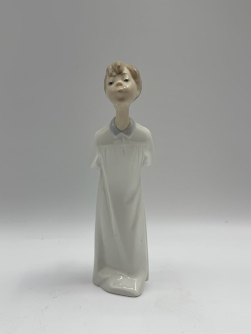 Lladro "Little Guest" Porcelain Figurine: Lladro porcelain figurine depicting a young boy in a nightshirt with his hands behind his back. Marked on the bottom. Stands approximately 10 inches tall.
