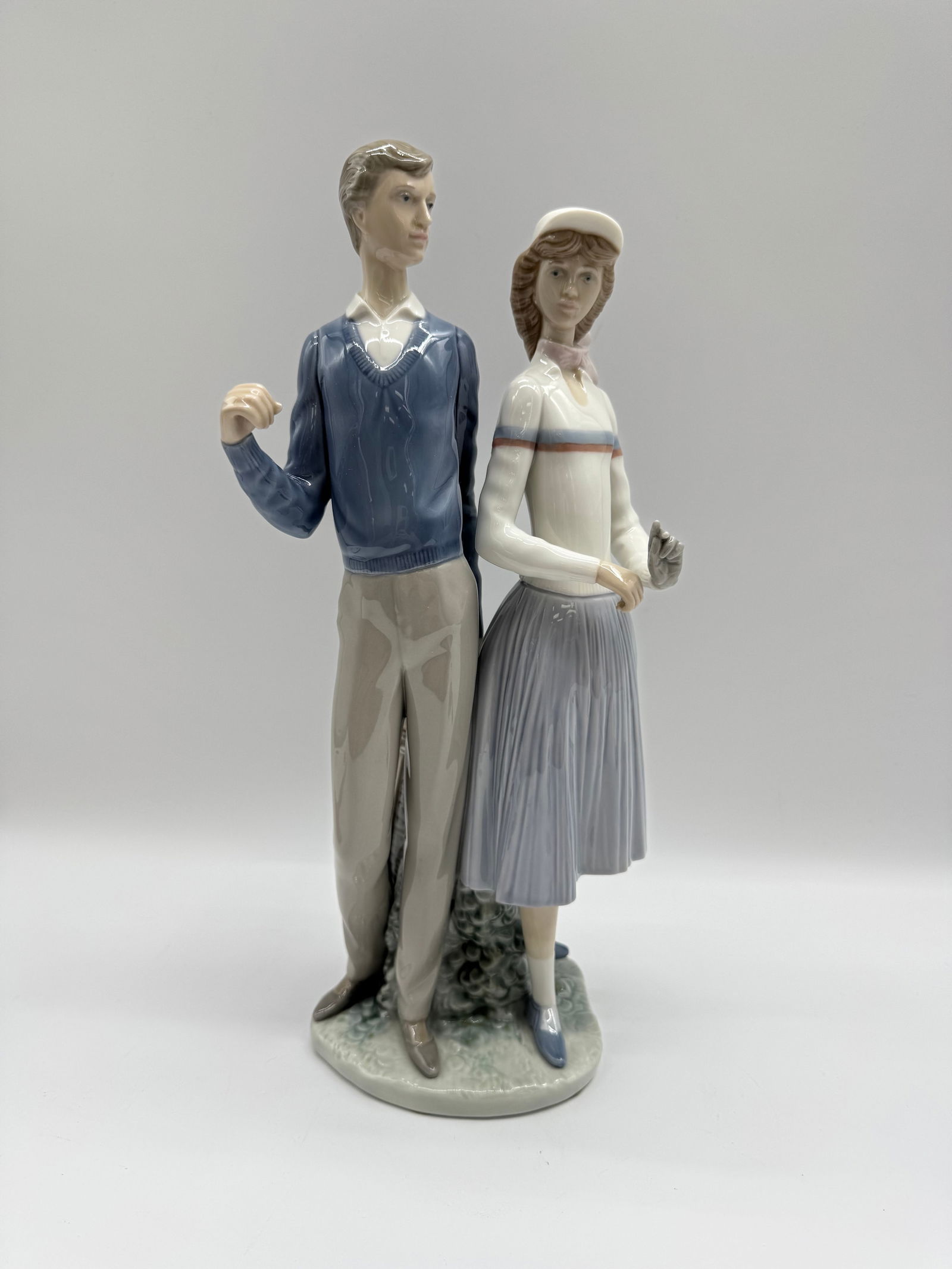 Lladro Figurine - Golfing Couple #1453: Lladro porcelain figurine depicting a golfing couple. The man is dressed in a blue sweater and khaki pants, while the woman wears a white top and blue skirt. Marked on the base. Measures approximately