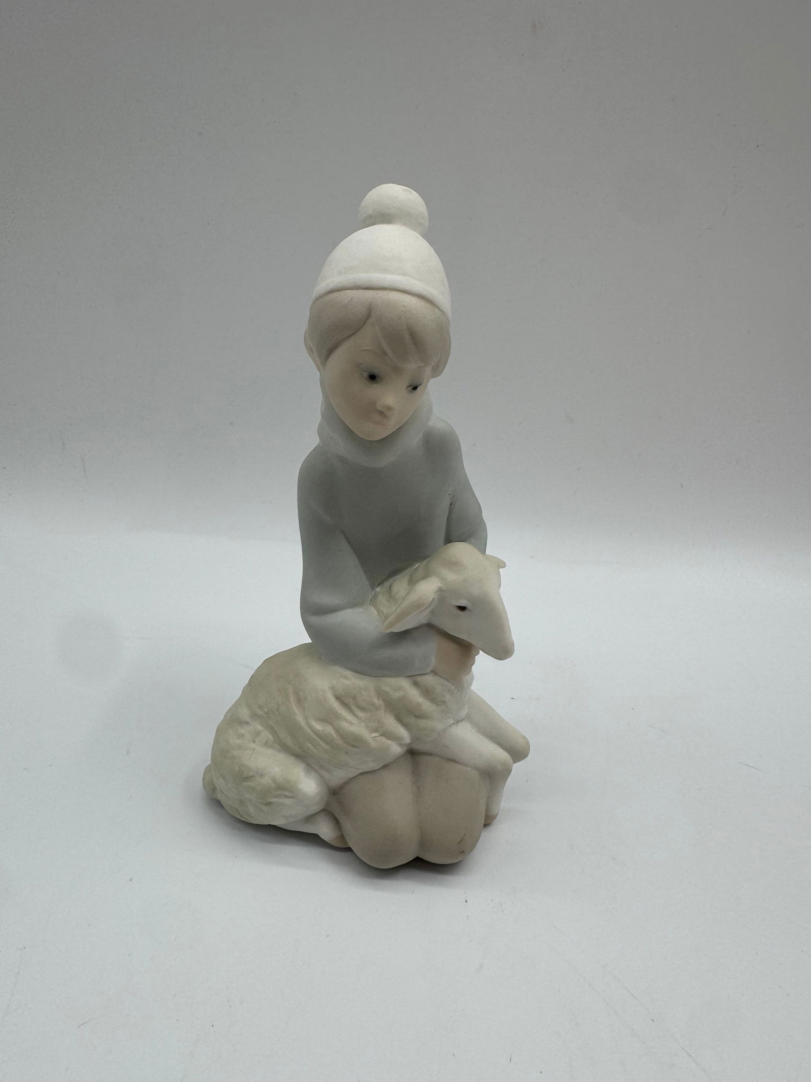 Lladro Figurine: Girl with Lamb: Lladro porcelain figurine depicting a young girl in a hat, cradling a lamb. Marked on the base. Soft, muted coloration. A charming collectible piece.