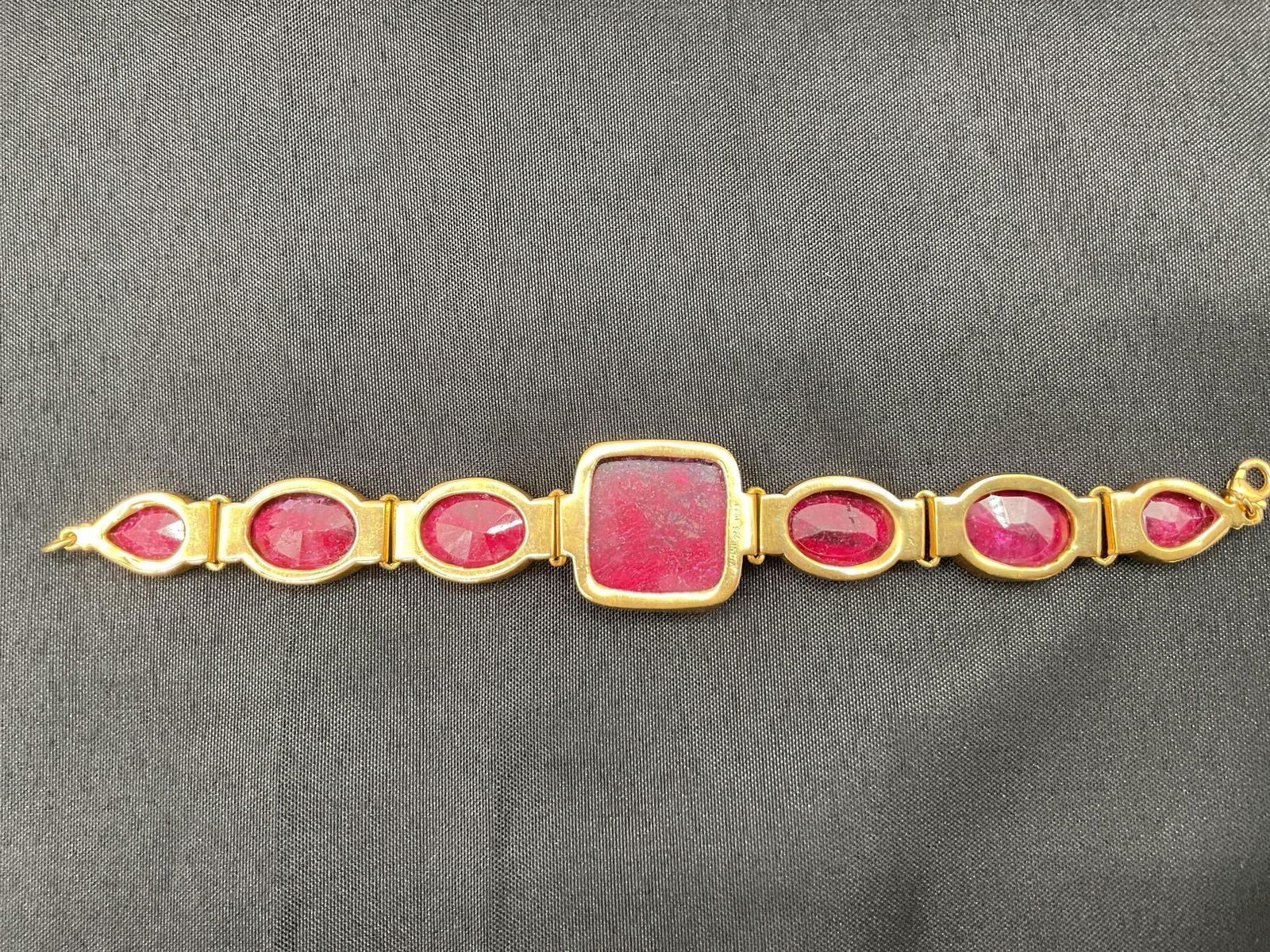 Indian Ruby Corundum Bracelet with 7 Faceted Stones: Handcrafted bracelet featuring 7 bezel-set faceted stones made from a ruby variety of corundum. Gold-tone metal setting, made in India. Dimensions: Length 7in Medium: Corundum (ruby) in gold-tone