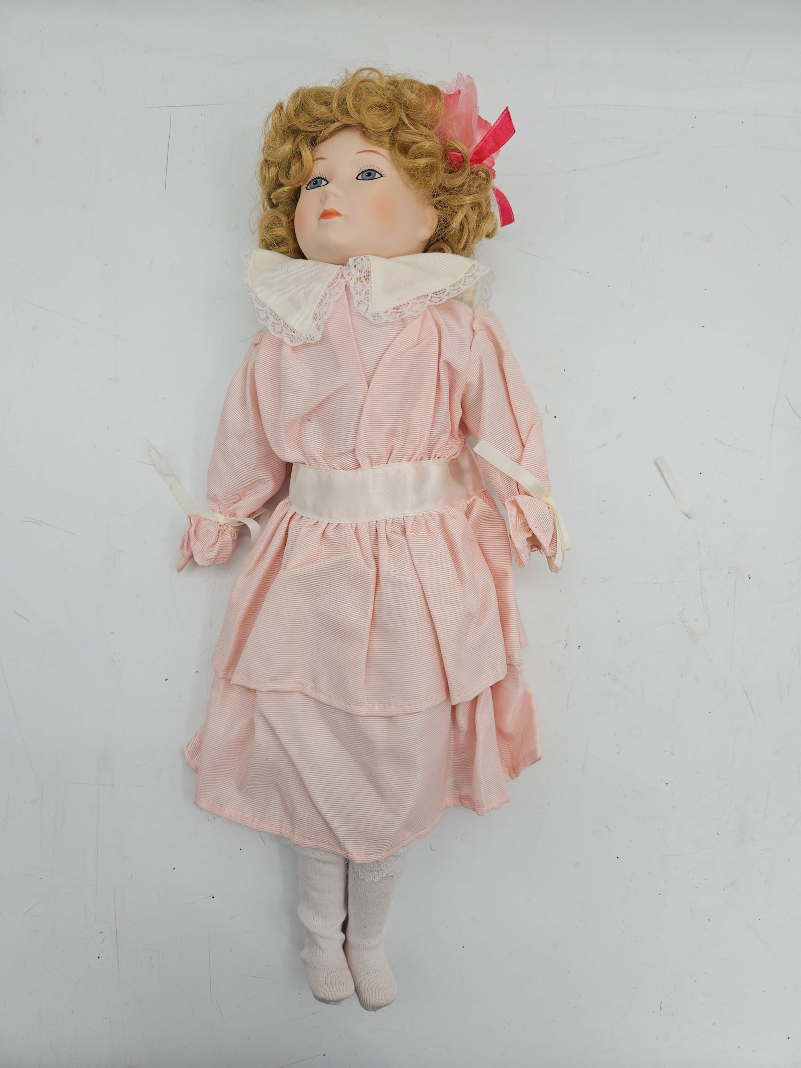 Antique Bisque Head Doll, Pink Dress, 18" Tall: Antique bisque head doll with curly blonde hair and blue eyes. Dressed in a pink dress with white accents and matching stockings. Measures approximately 18 inches tall and 8 inches wide at the widest