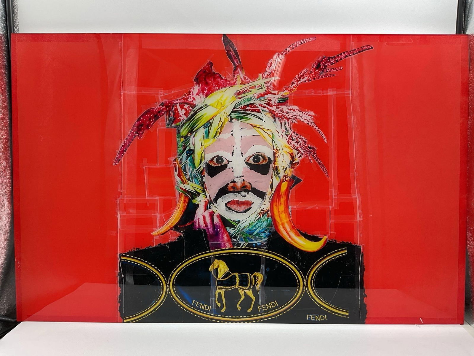 Fendi Flames by Carlos Felix (Mexico, B. 1981): Bold mixed media collage featuring a white-masked face with multicolored hair set against a vivid red backdrop. Iconic Fendi branding and horn-like accents evoke a blend of fashion, fantasy, and rebel