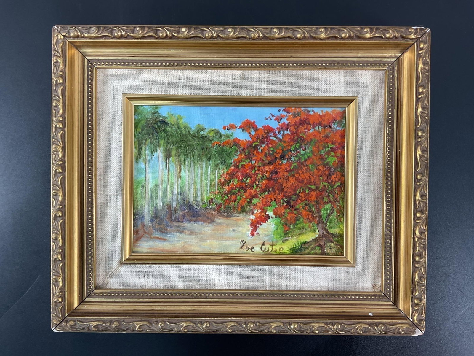 Maria Callas (American, 1923-1977) Oil on Canvas: This vibrant painting features a tropical landscape with a striking red-flowered tree, likely a Royal Poinciana, set against a backdrop of tall, slender palm trees. The artist has skillfully used brig