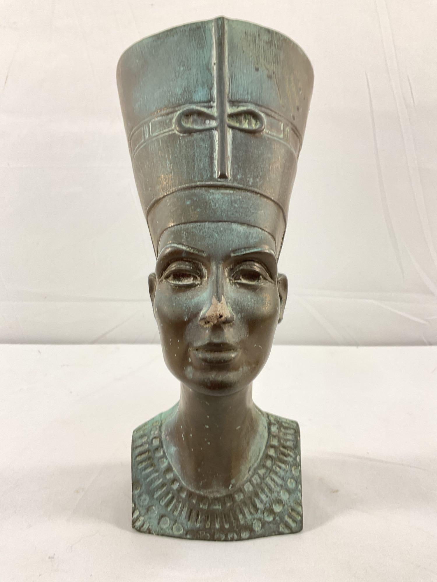 Bronze Bust of Queen Nefertiti: A finely detailed bust depicting Queen Nefertiti, the famous 18th Dynasty Egyptian queen. The piece showcases her signature tall, flat-top headdress with an intricate ribbon design. The patina and wea