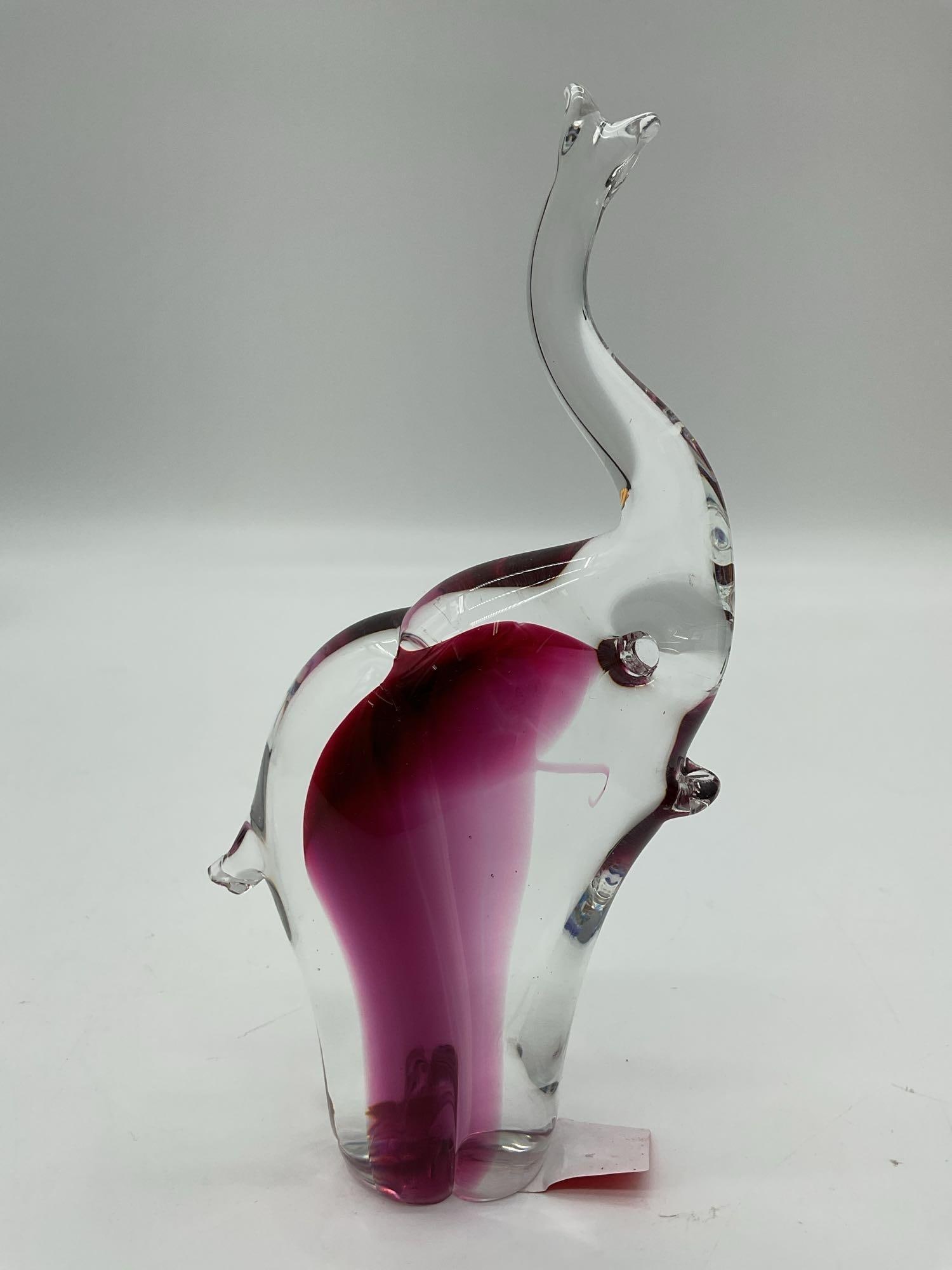Murano Style Art Glass Elephant Figurine: Elegant hand-blown glass elephant with a clear outer form and vibrant magenta-red core. Features a raised trunk symbolizing good luck. Likely inspired by or in the style of Murano glass. Dimensions: H
