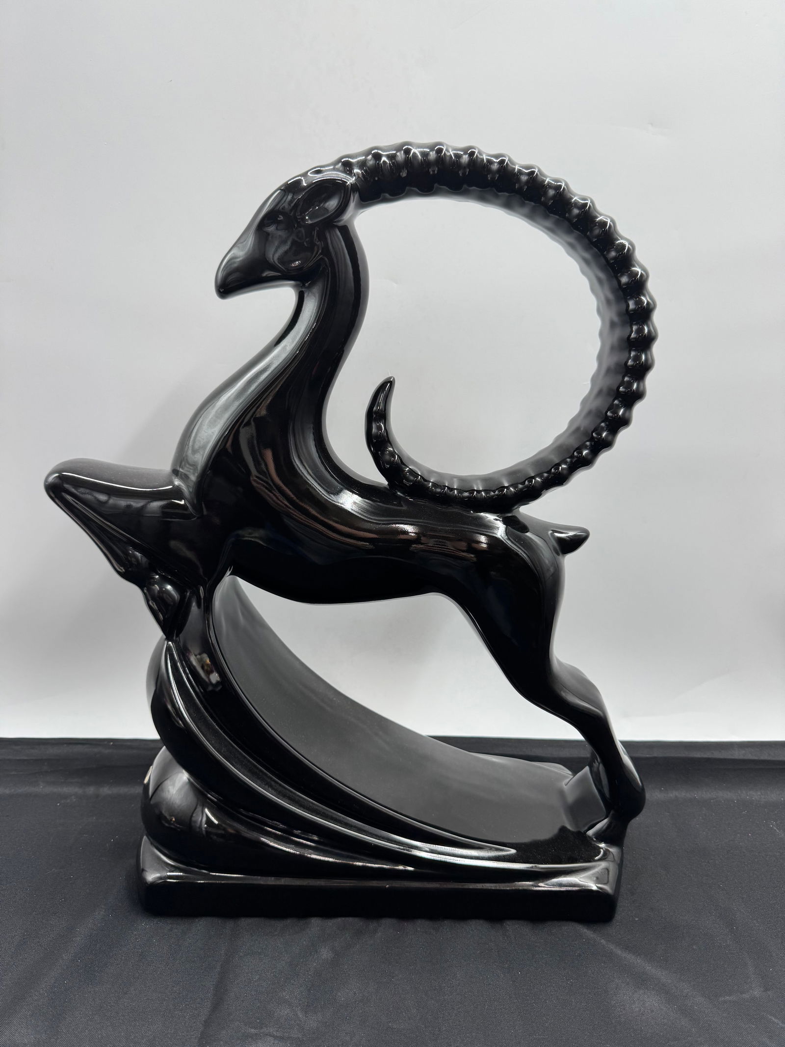 Black Ceramic Ibex Sculpture: A striking black ceramic sculpture depicting an ibex. The piece features a stylized design with curved horns and a sleek, modern aesthetic. Dimensions: L: 12in H:19in W:6in