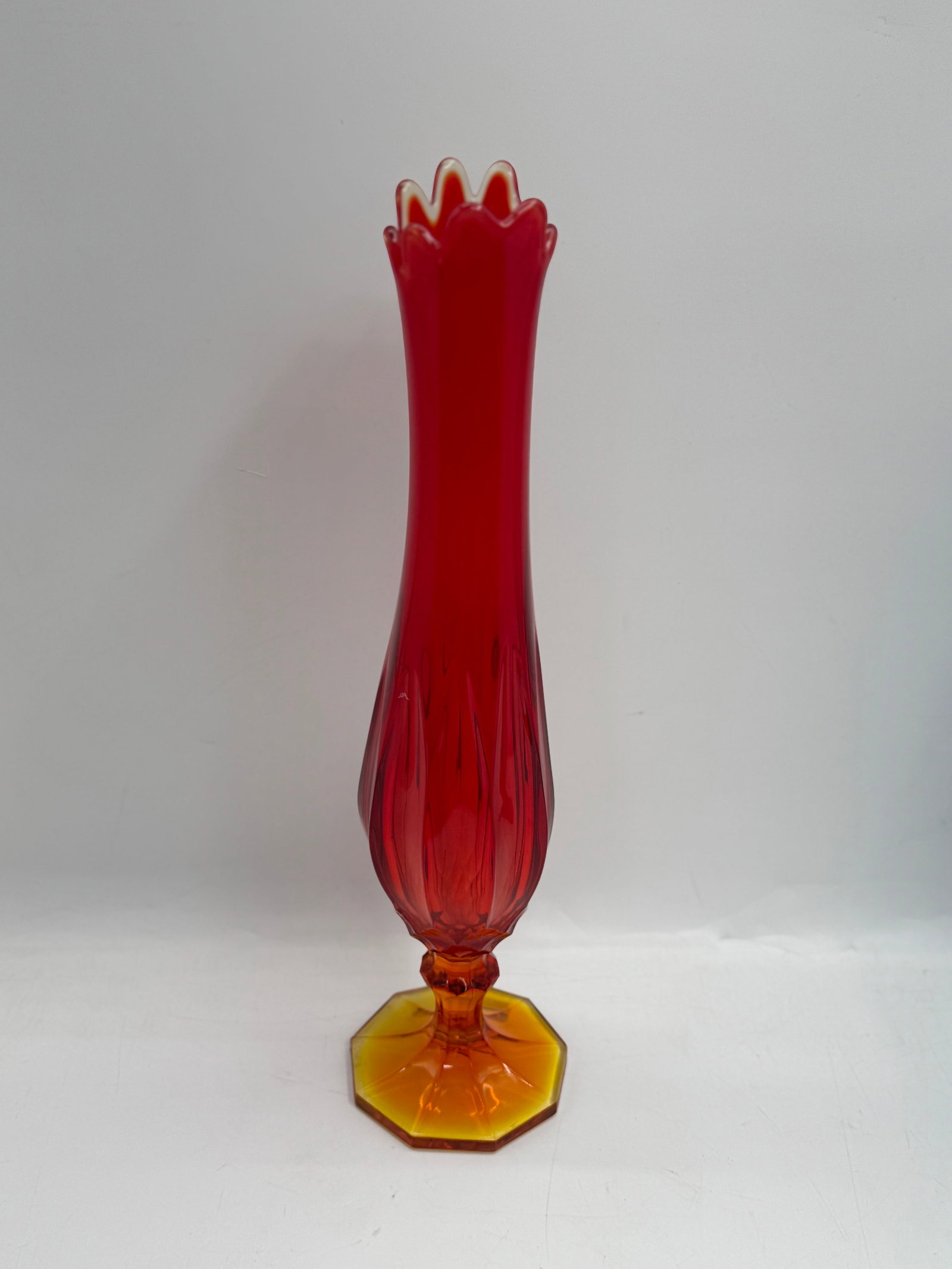 Red and Amber Swung Glass Vase with Fluted Rim: Tall red swung glass vase with a fluted rim and amber glass base. The vase features vertical ribbing and a bulbous midsection. Measures approximately 19 inches in height and 4.5 inches in width.