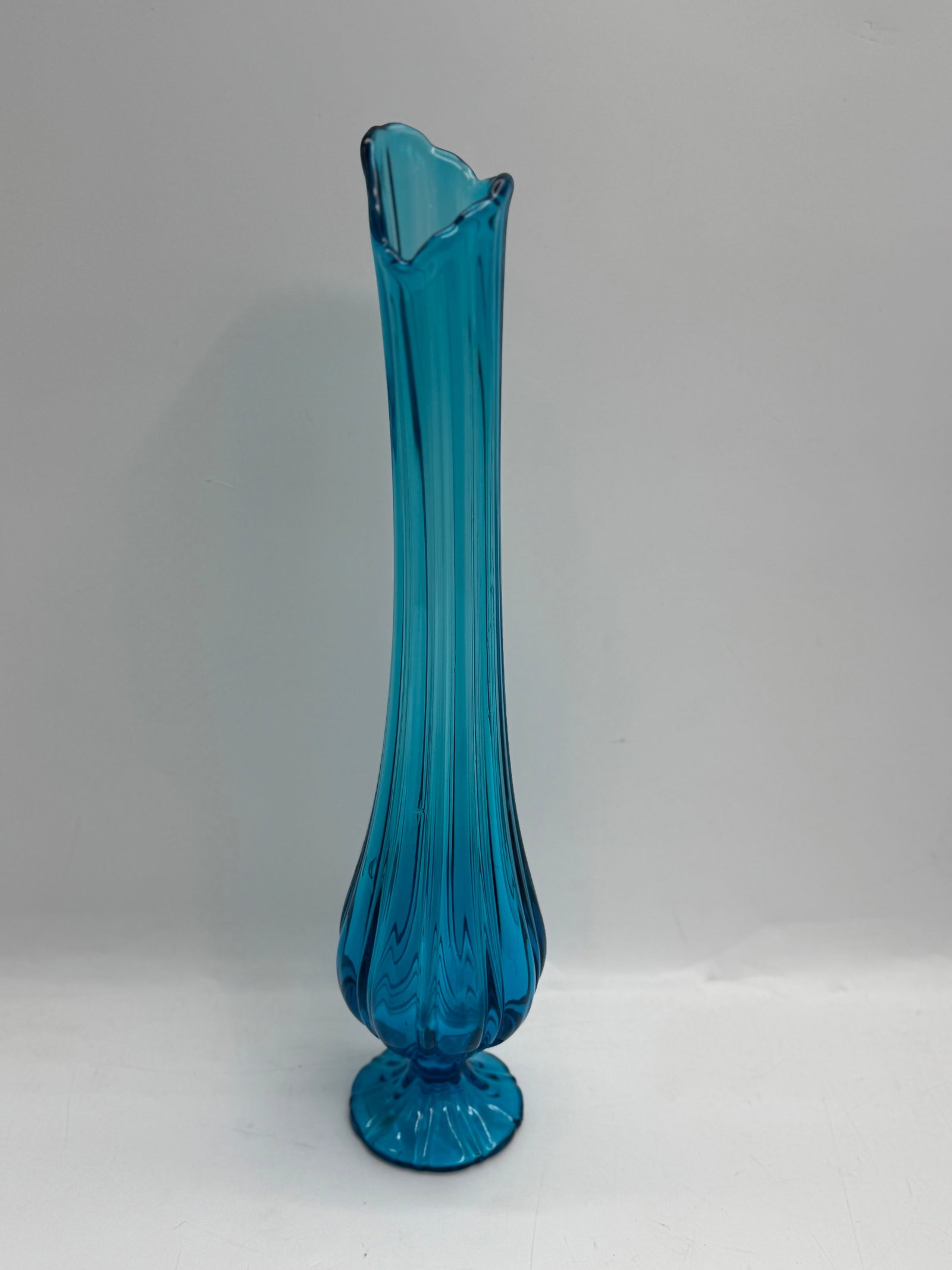 Vintage Turquoise Blue Swung Glass Vase: Tall, slender turquoise blue swung glass vase. Features a flared rim and a decorative base. Measures approximately 19 inches tall and 5 inches in diameter at its widest point. A striking decorative pi