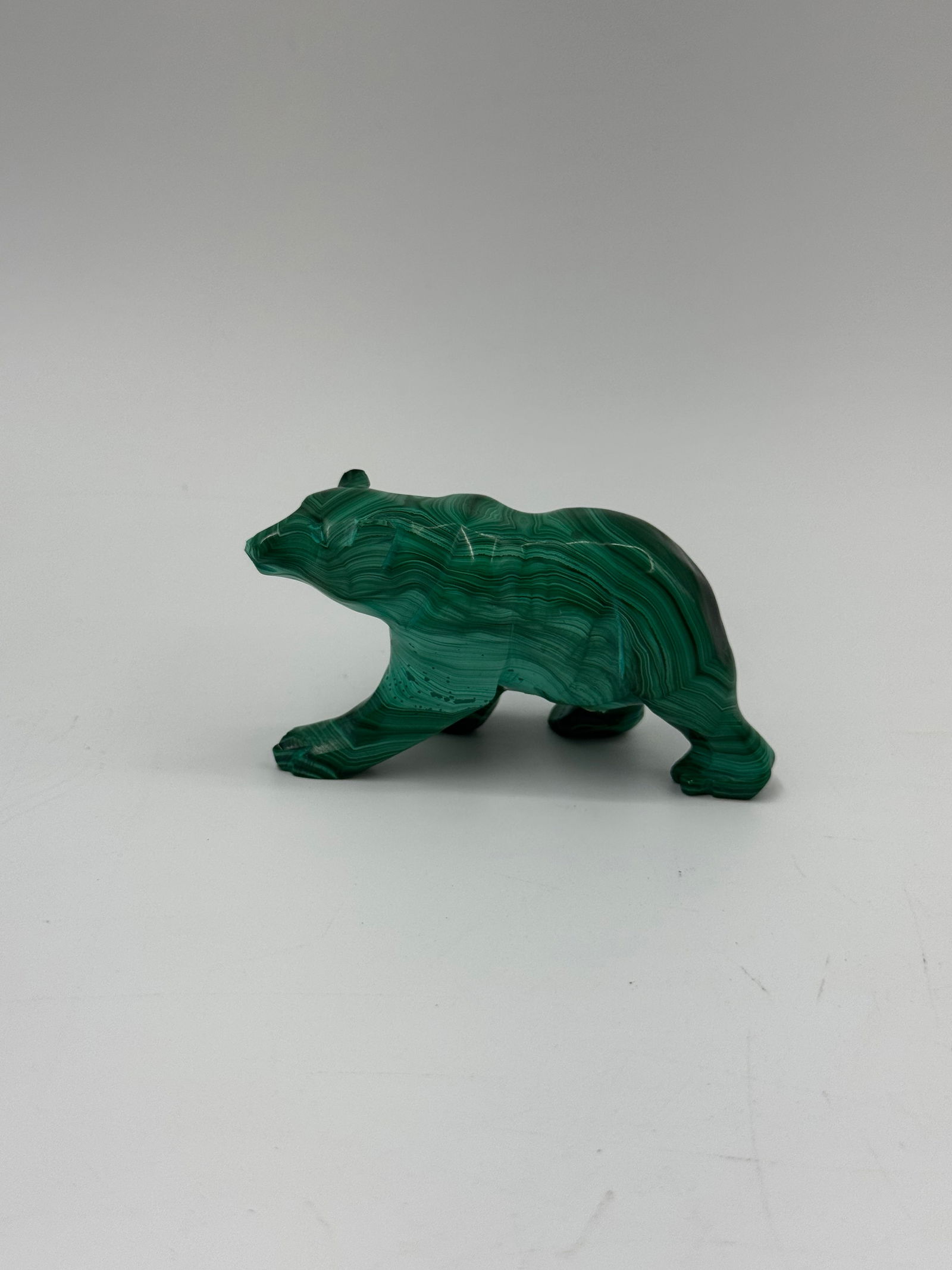 Malachite Bear Carving: A small carving of a bear, crafted from malachite. The piece measures approximately 3 inches in length and 1.5 inches in height. The malachite displays its characteristic green banding and patterns. A