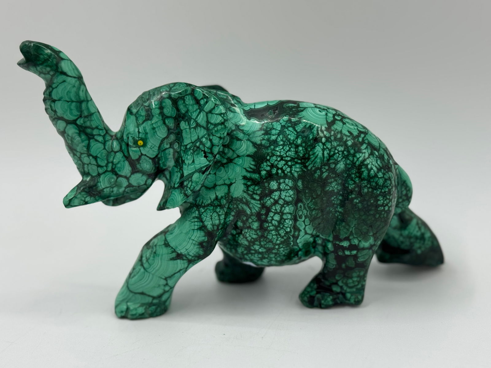 Malachite Elephant Carving: A carved elephant figurine made of malachite. The piece measures approximately 7.5 inches in length, 5.5 inches in height, and 2 inches in width. The elephant is depicted with its trunk raised. The ma