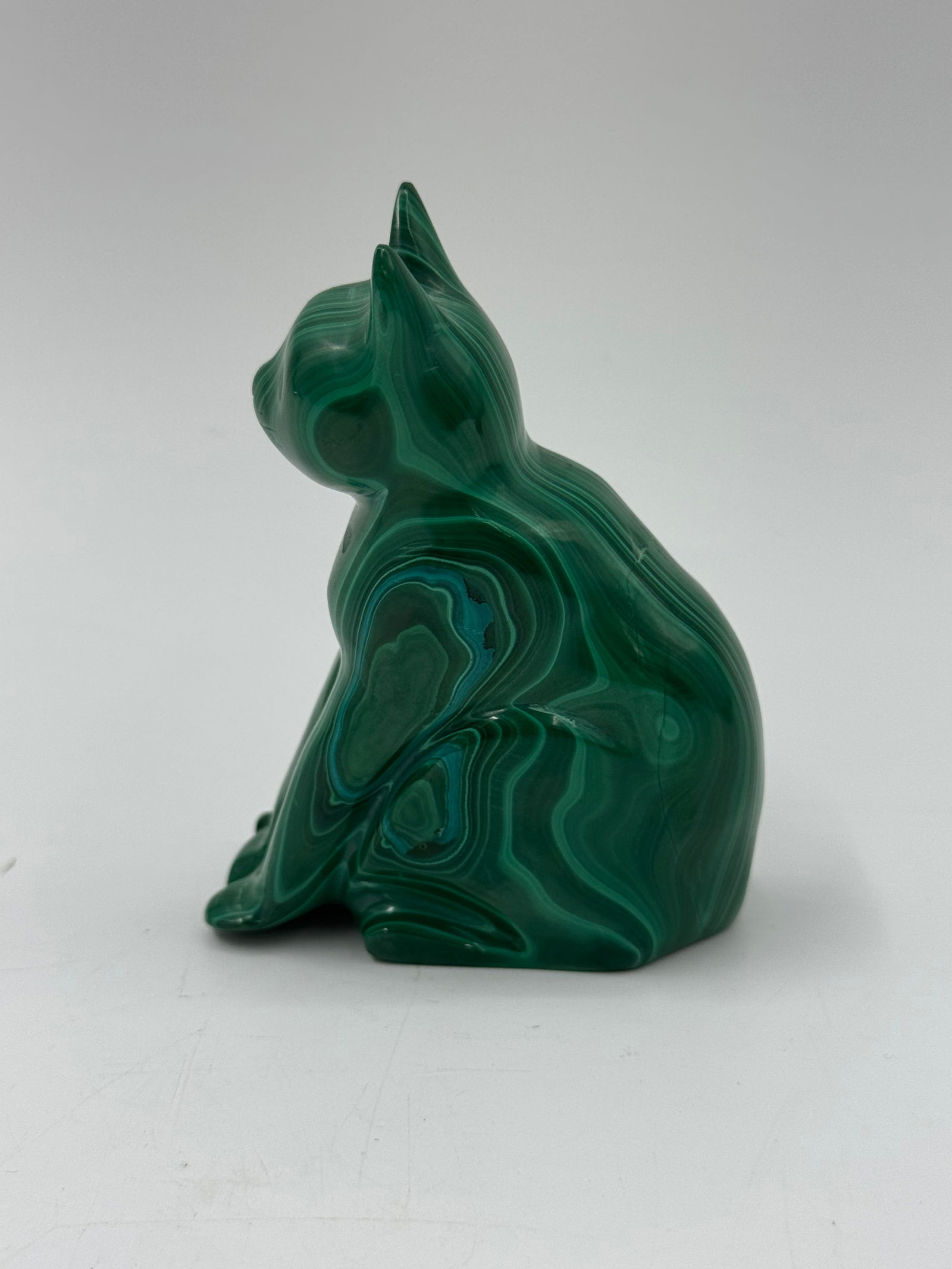Malachite Cat Sculpture: A carved malachite sculpture depicting a cat in a resting pose. The piece showcases the natural banding and rich green hues characteristic of malachite. Dimensions: 3.5 x 3 x 1 inches.