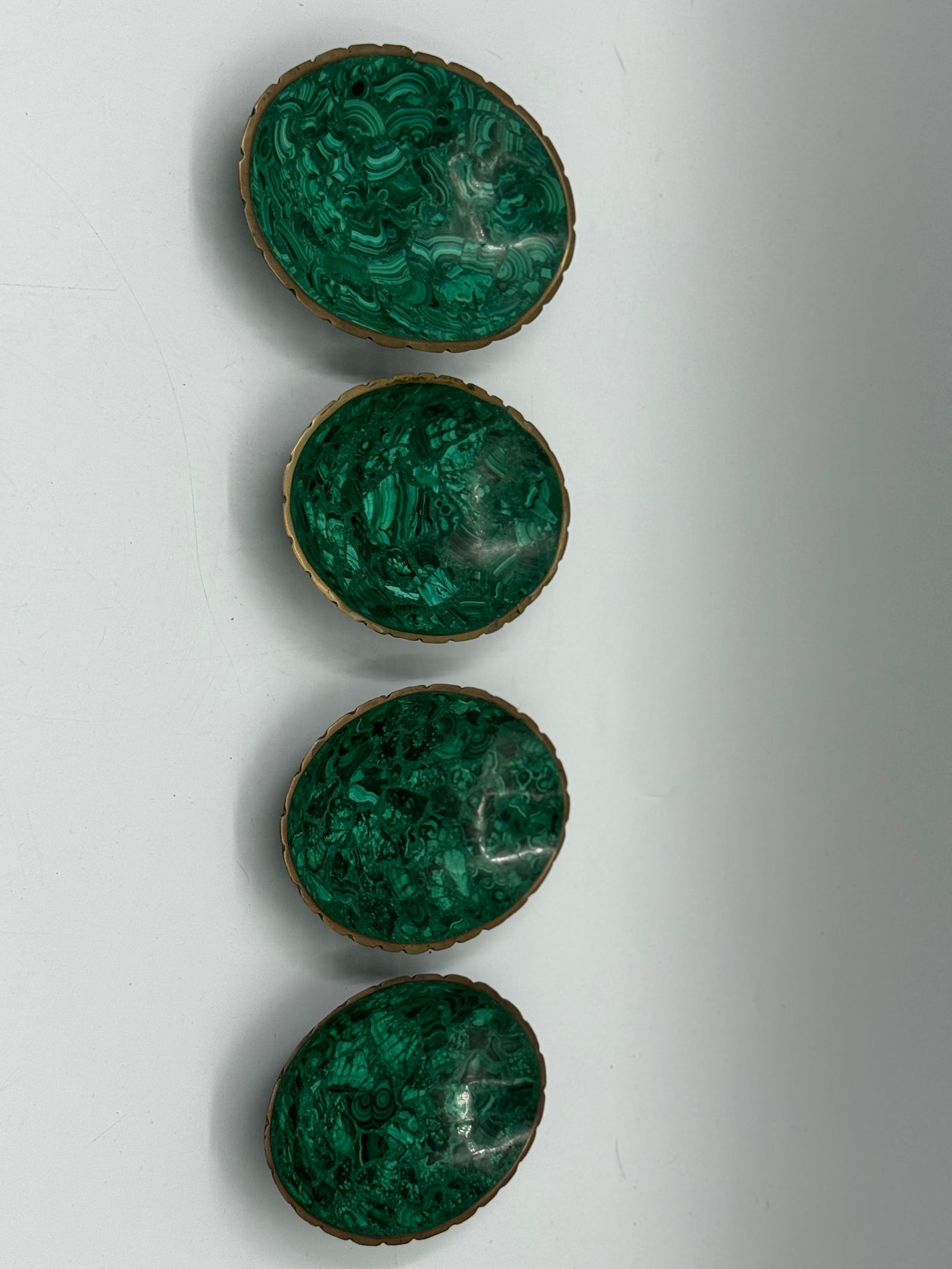 Set of Four Malachite Cabochons in Metal Bezels: Set of four oval malachite cabochons, each set in a decorative metal bezel. The stones exhibit characteristic banding and rich green hues. 6x4.5in