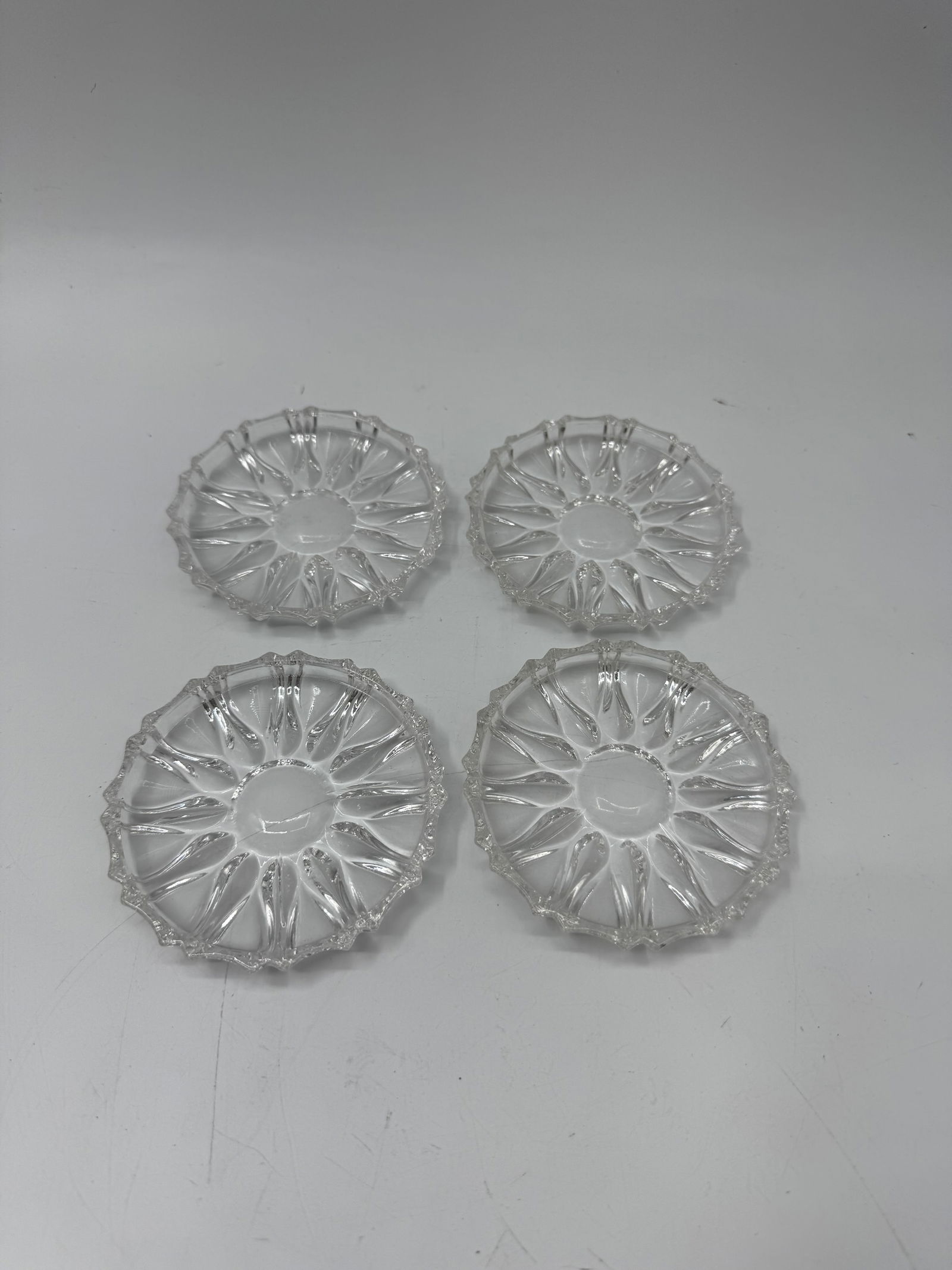 Set of Four Pressed Glass Coasters: Set of four pressed glass coasters, each approximately 4 inches in diameter. The coasters feature a sunburst pattern. Suitable for protecting furniture surfaces.