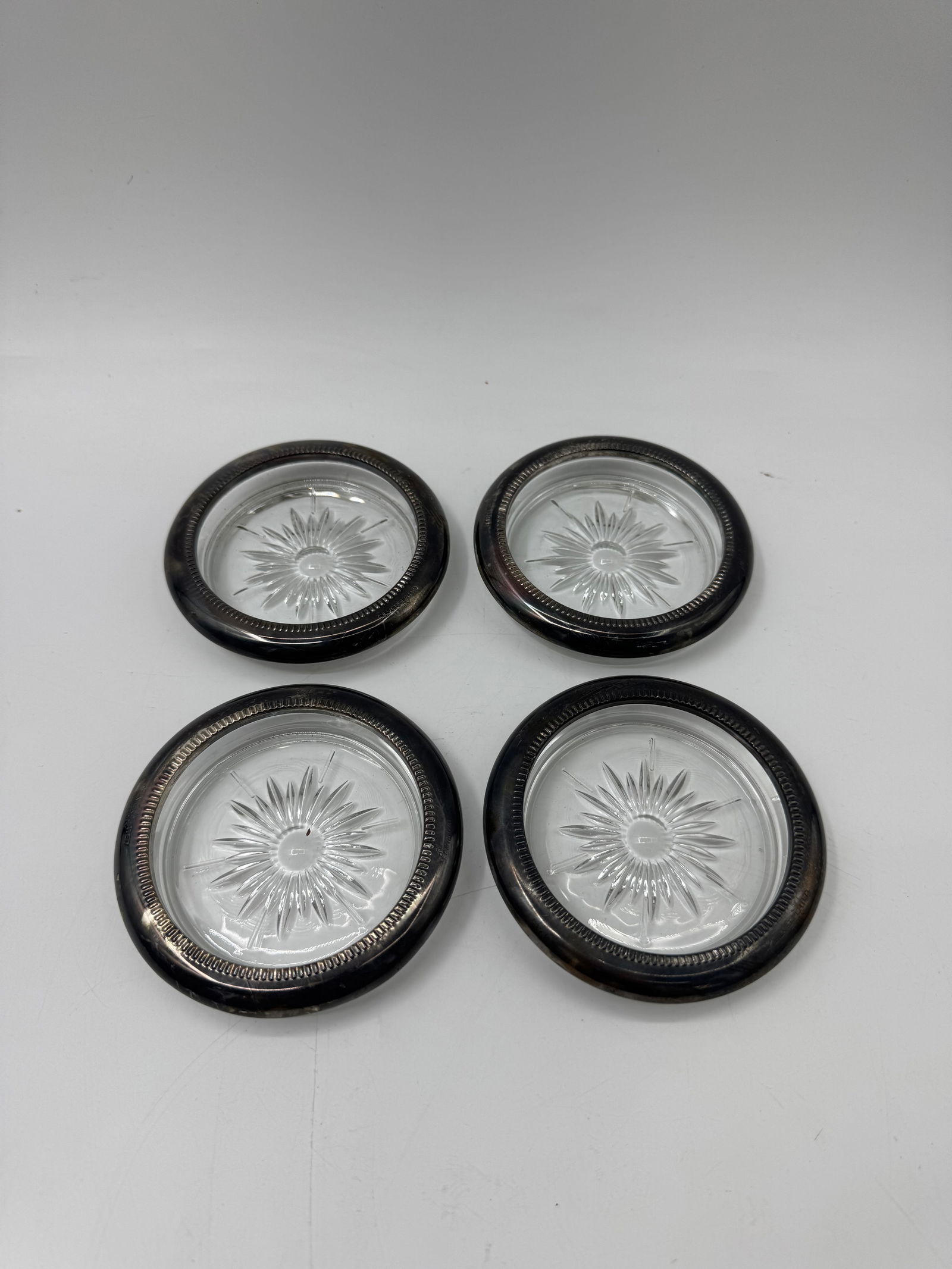 Set of Four Silver Rimmed Glass Coasters: Set of four glass coasters with silver rims. Each coaster measures approximately 4 inches in diameter and features a starburst design on the glass.