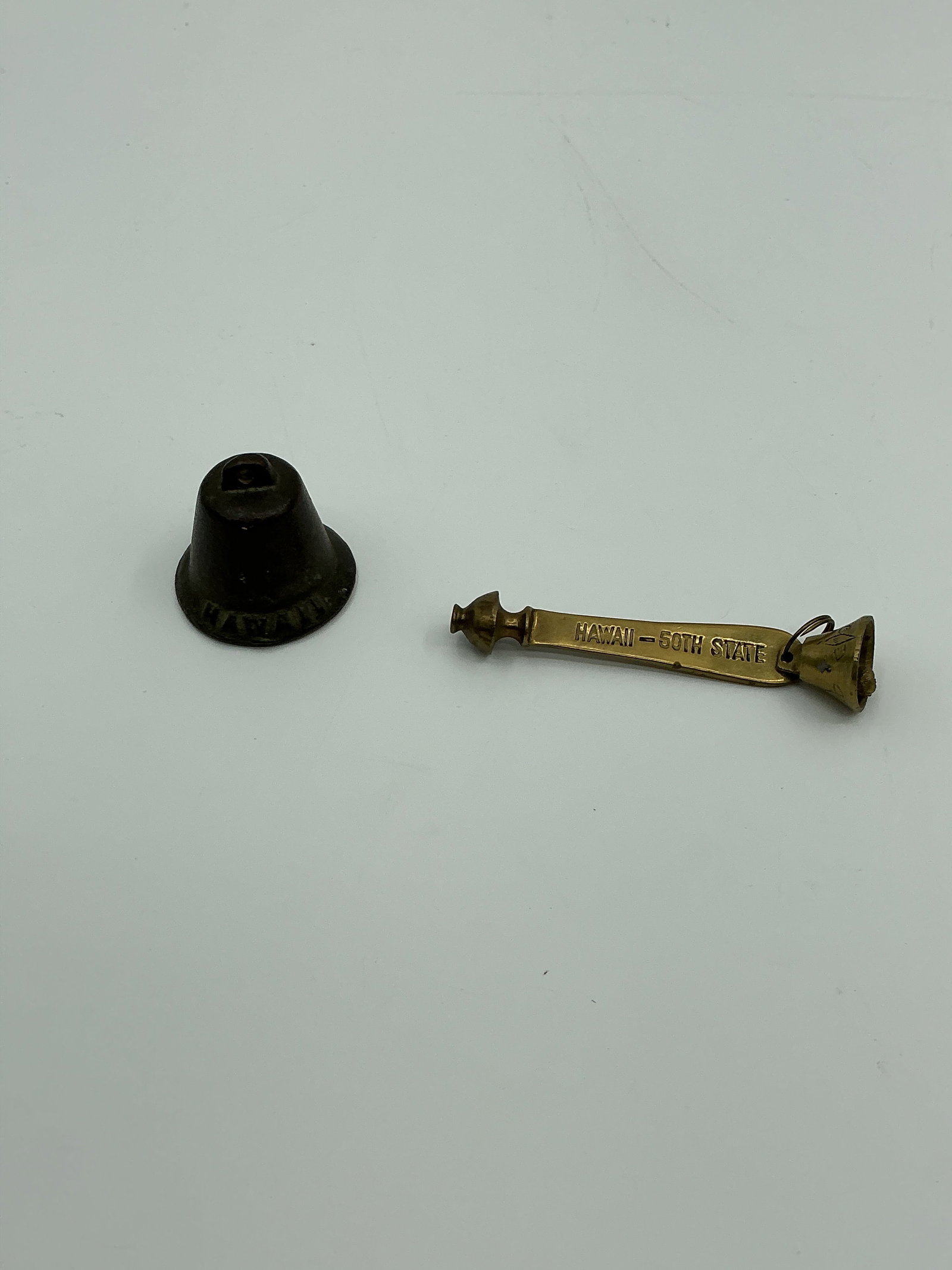 Two Hawaii Souvenir Bells: Two souvenir bells, one 1.5 in height and 1.5 inch diameter and the other 4 inches long, both marked 'Hawaii'.