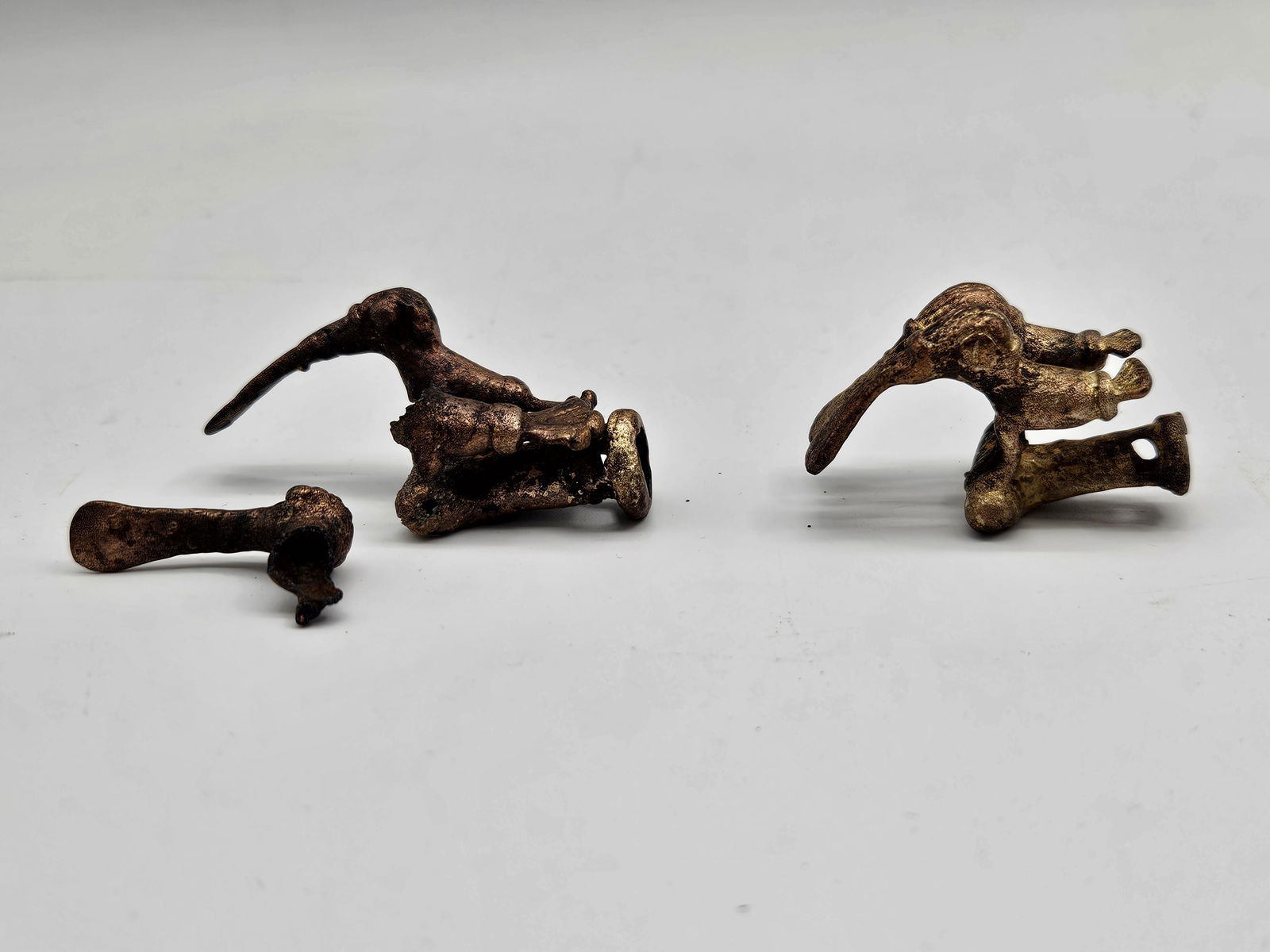 Three Bronze Figural Fragments: Three bronze fragments, possibly from larger figural sculptures or decorative objects. The fragments show varying degrees of detail and oxidation, suggesting age and exposure. One appears to be a hand