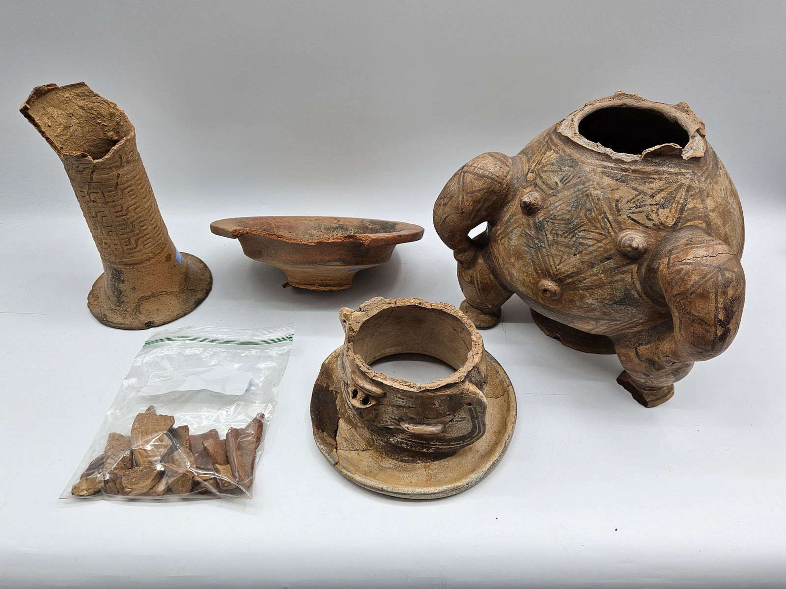 Pre-Columbian Pottery Vessels and Fragments: Collection of Pre-Columbian pottery vessels and fragments. Includes a large vessel with applied decoration, a bowl, a collared vessel, and other fragments. Condition varies, with significant losses an
