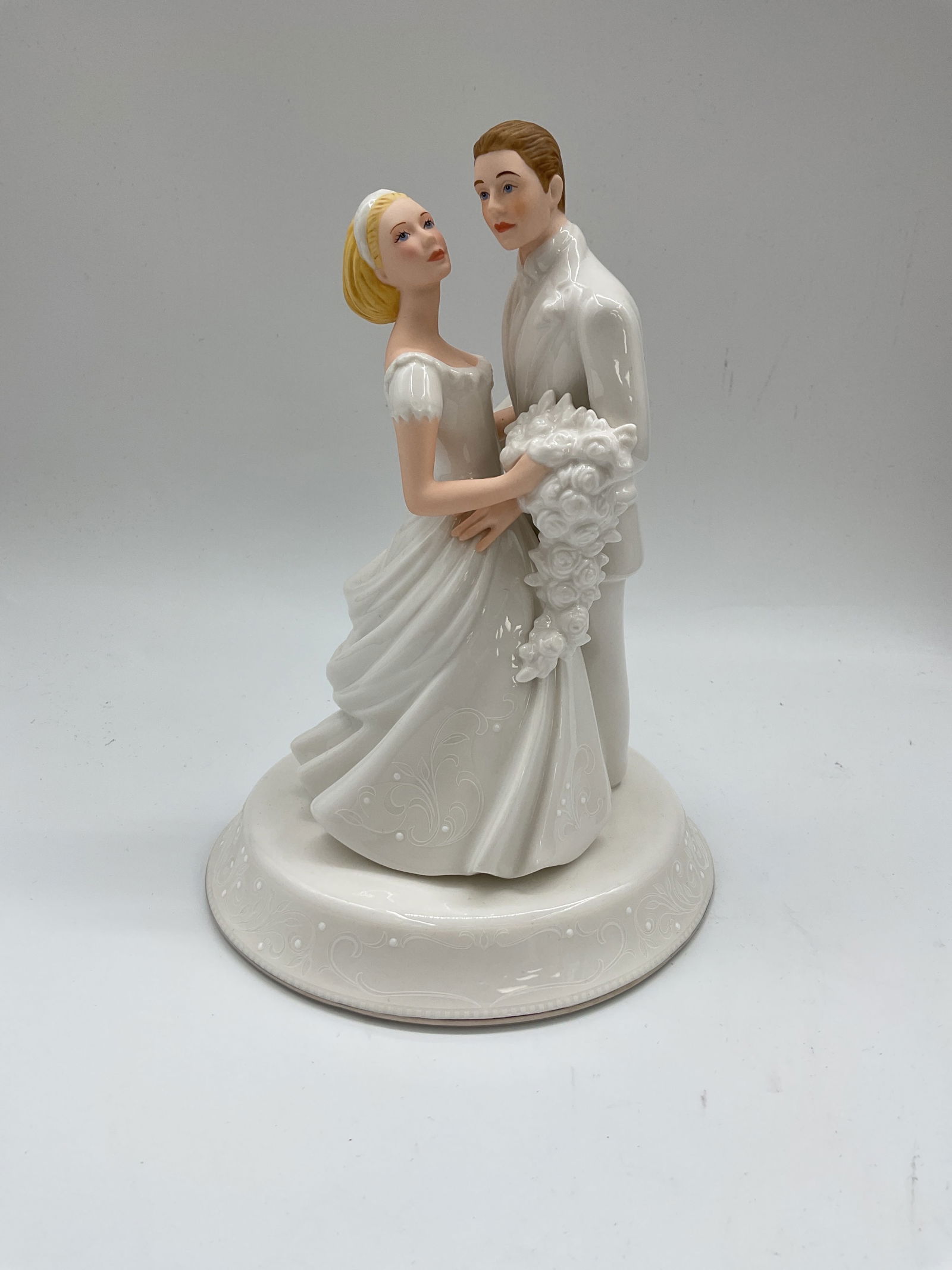 Lenox Bride and Groom Figurine: Elegant porcelain figurine from the Lenox Wedding Promises Collection depicting a bride and groom in a romantic embrace. The bride holds a cascading bouquet while gazing lovingly at the groom in a whi