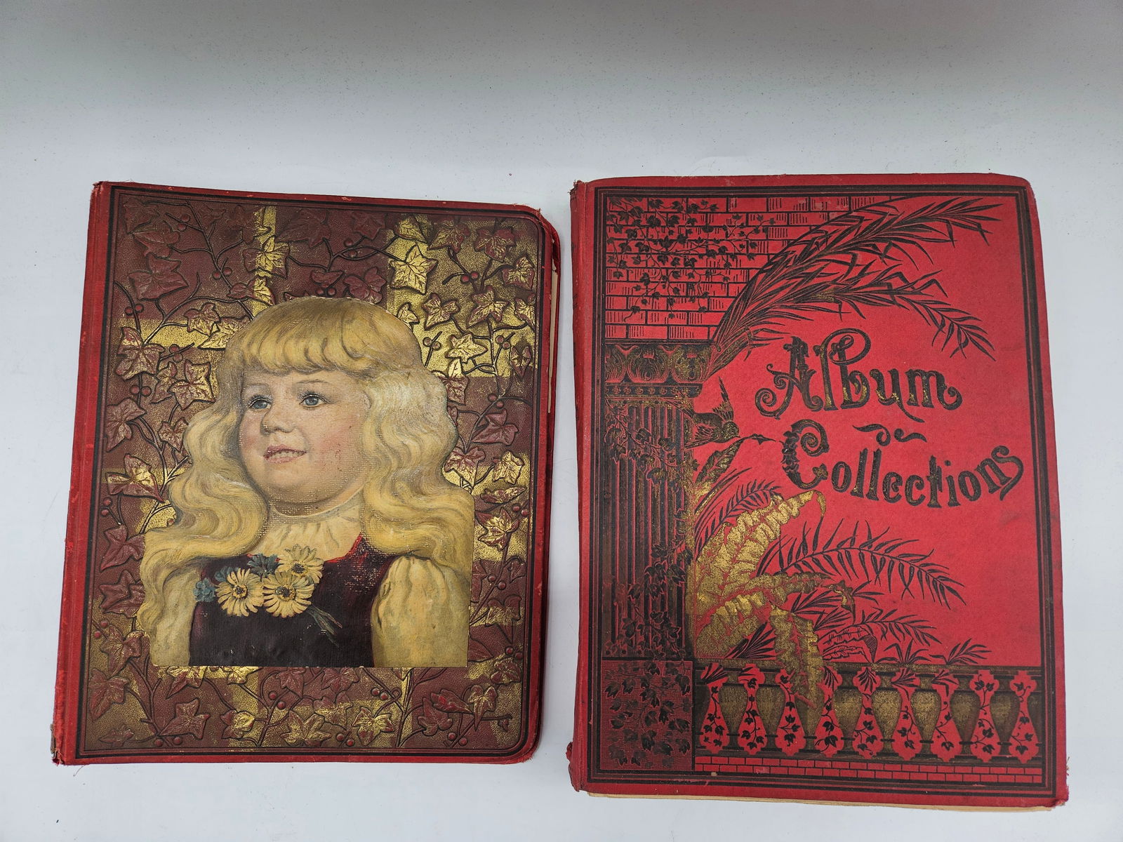 Victorian Trade Card Albums (Pair): Two antique 19th-century albums filled with original Victorian trade cards, chromolithographs, and ephemera. The covers feature ornate embossed and gilded designs, one depicting a young girl and the o