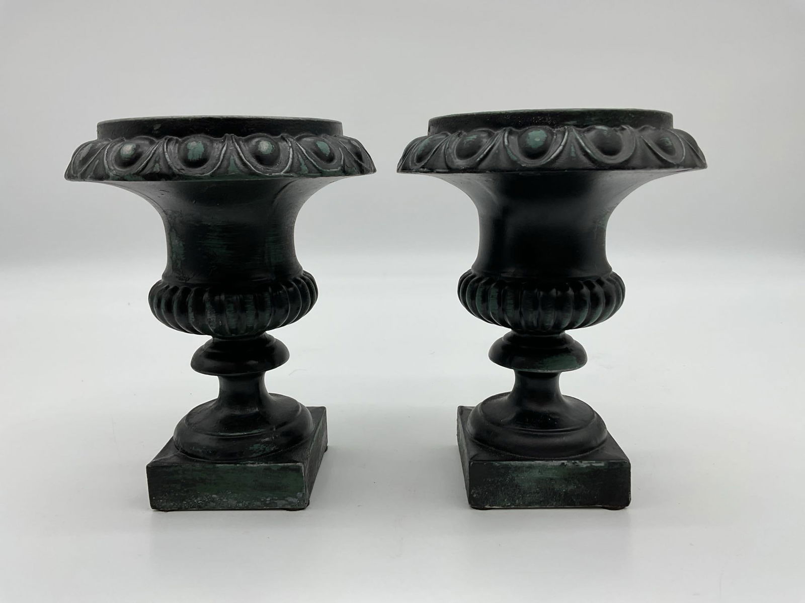 Pair of Decorative Cast Iron Urns with Acanthus Detail: Compact vintage-style cast iron urns featuring a classical design with acanthus leaf patterns along the rim and a square pedestal base. Finished in black with a green patina for an aged look, ideal fo
