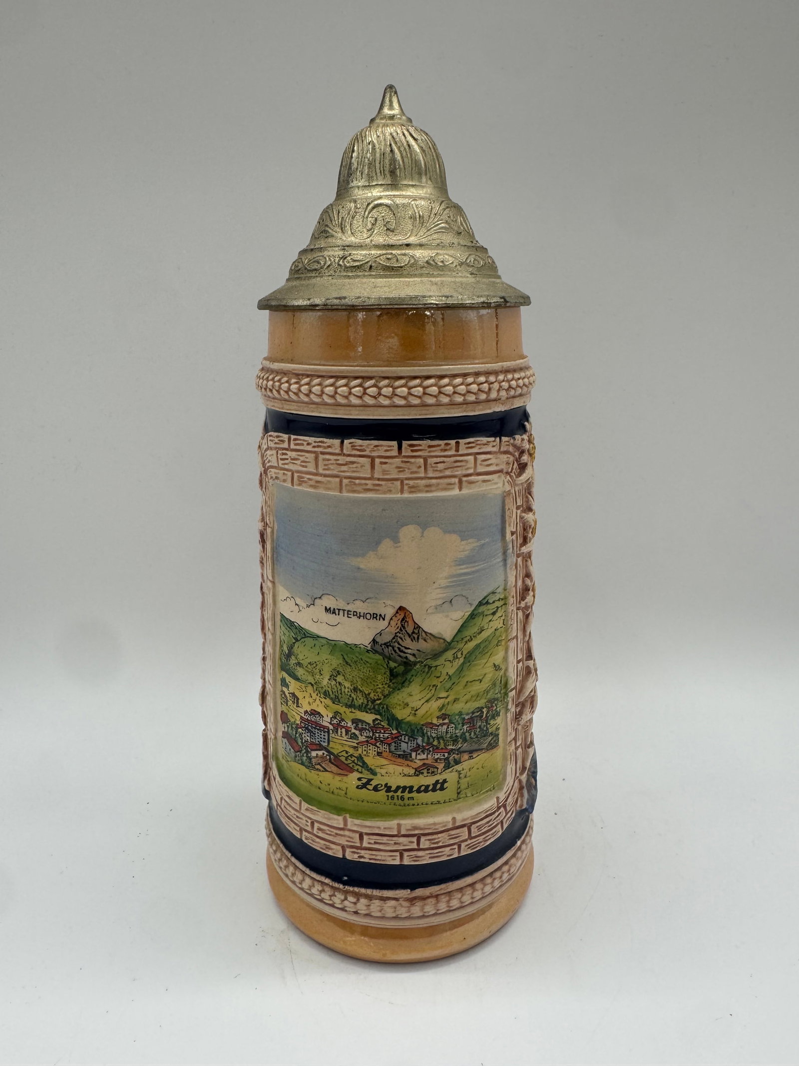 Zermatt Switzerland Lidded Souvenir Beer Stein with Alpine Scenes: Attractive lidded souvenir beer stein from Zermatt, Switzerland, featuring colorful raised alpine scenes. One panel shows a panoramic view of the village and surround