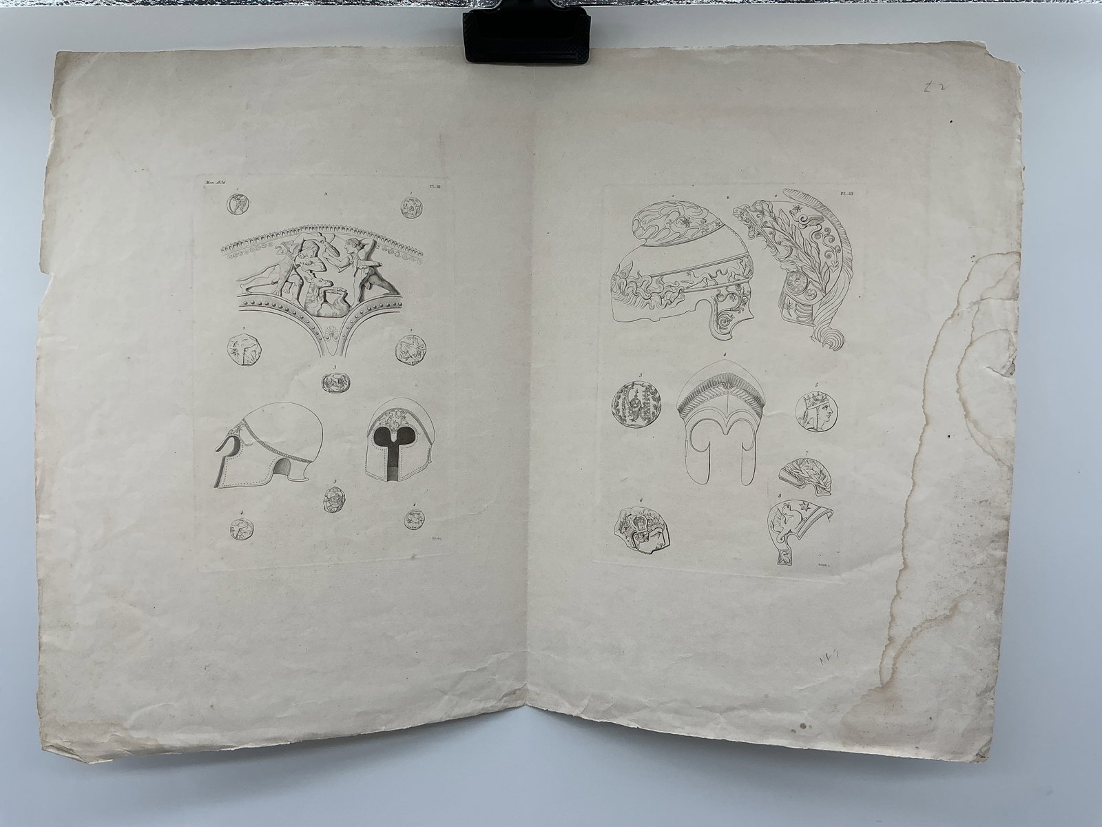 Antique Print of Ancient Helmets and Coins: Antique print featuring detailed illustrations of ancient helmets and coins. The print showcases various helmet designs and coin profiles, offering a glimpse into historical armor and currency. Likely