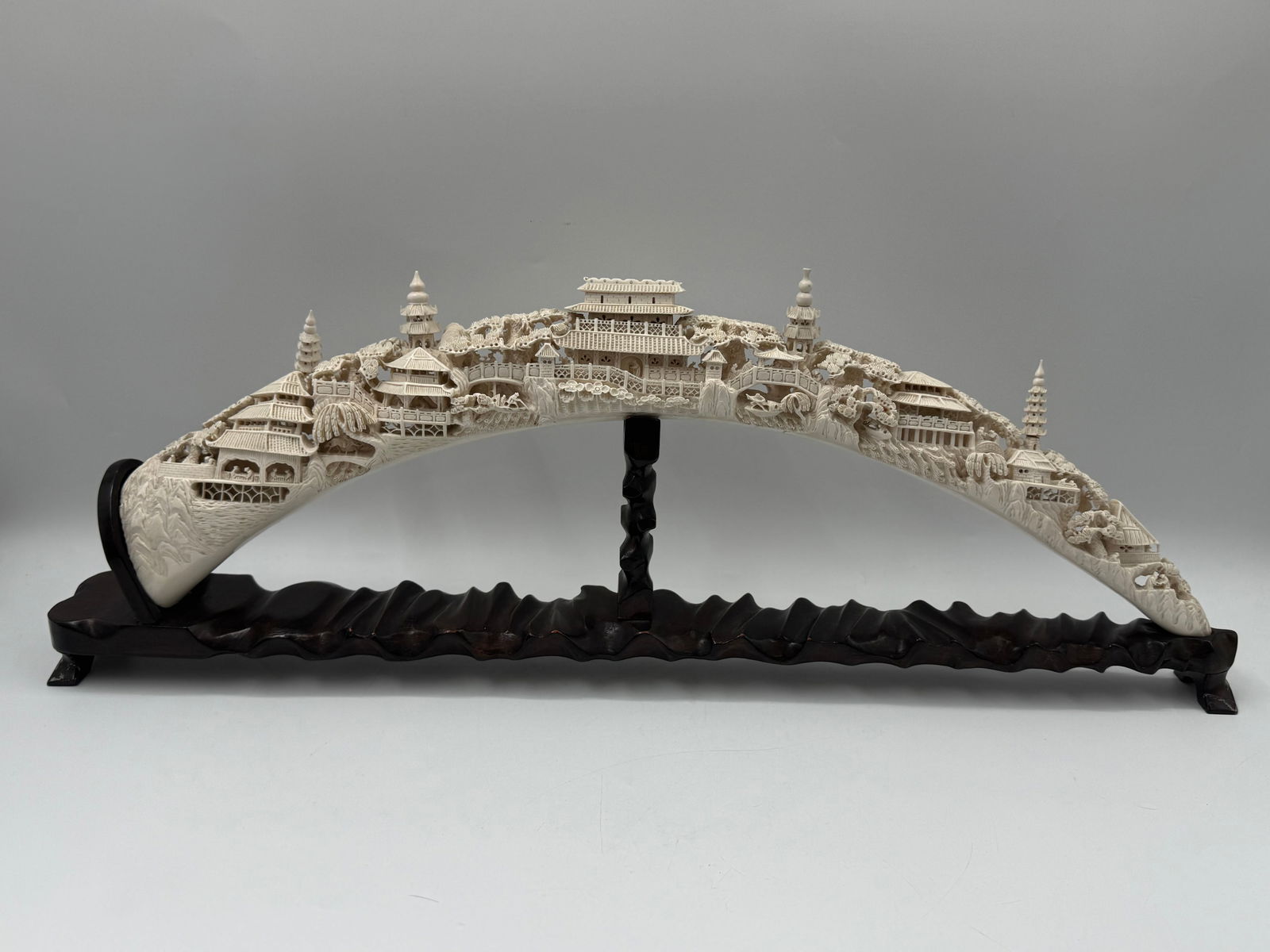 Carved Asian Cityscape on Stand: Unique piece depicting an elaborate Asian cityscape, featuring detailed buildings, pagodas, and bridges. This is mounted on a carved wooden stand. Dimensions: 32 x 11 x 3 inches.