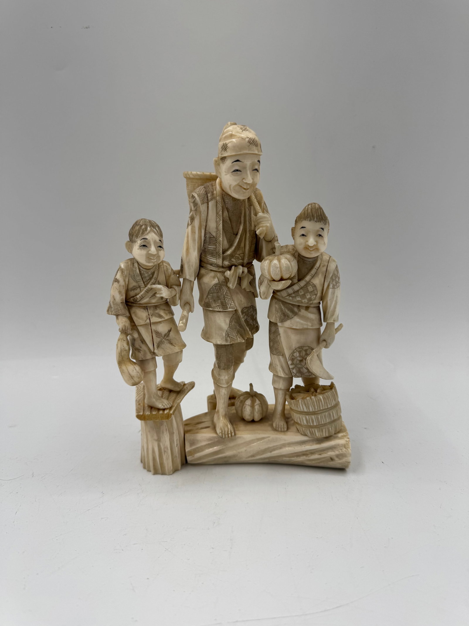 Japanese Okimono of Man and Children: A carved bone okimono depicting a man with two children. The figures are intricately detailed with realistic features and clothing. The sculpture measures 8.5 x 5.5 x 3 inches. Good overall condition.