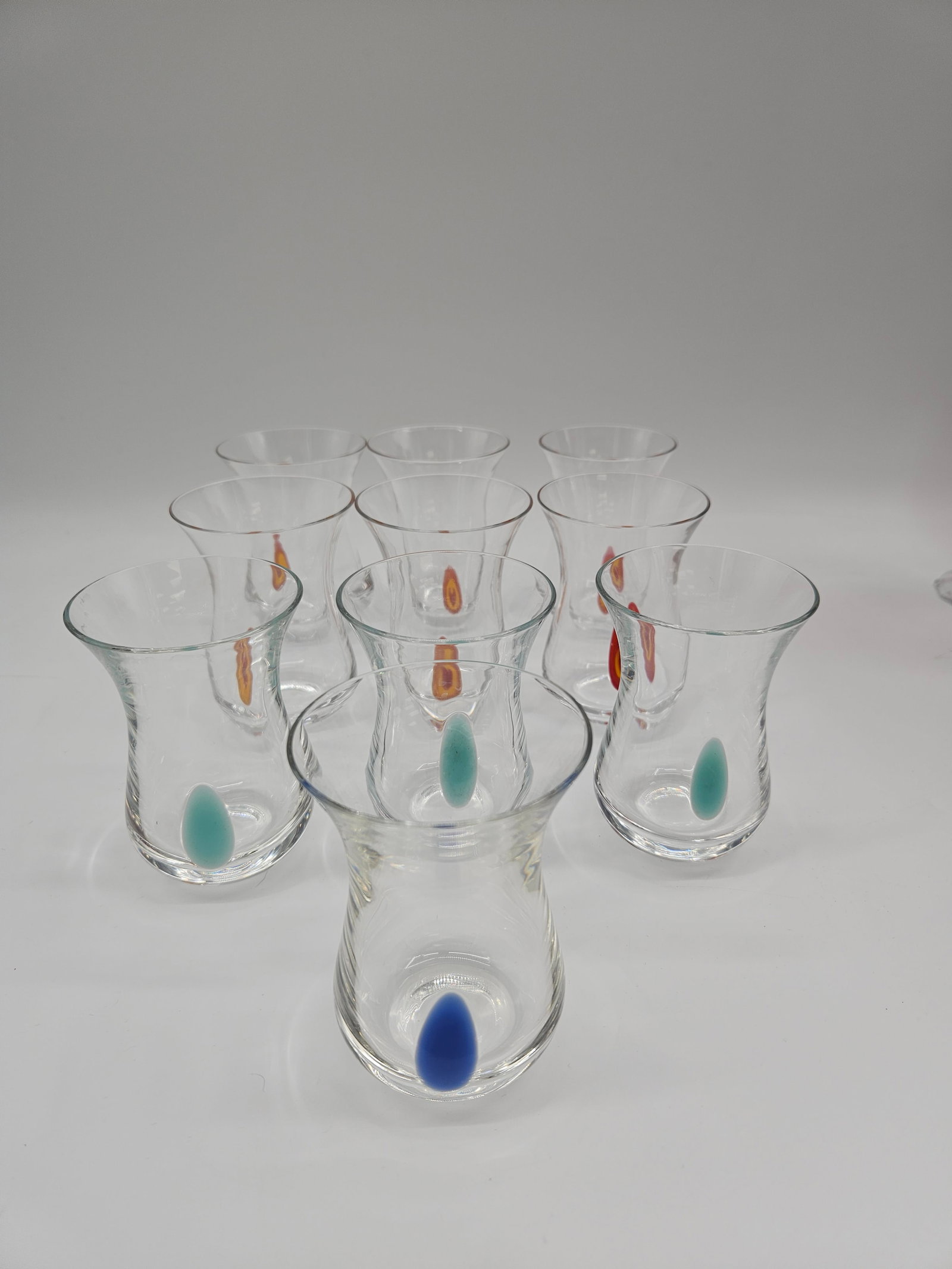 Set of 10 Glass Tumblers with Colored Teardrop Design: Group of 10 clear glass tumblers, each featuring an inset colored teardrop design. Approximate size 4 inches high by 2 1/2 inches in diameter.