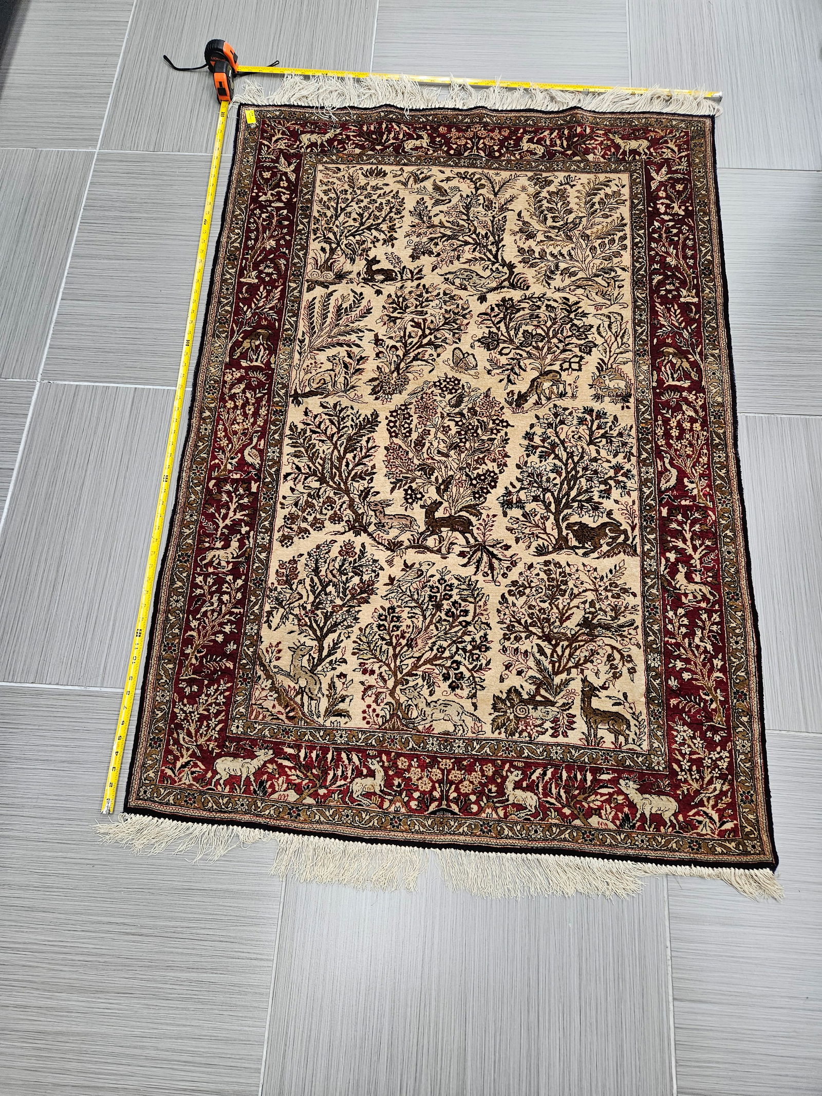 Handwoven Tree of Life Persian Rug: A finely detailed handwoven Persian rug featuring the classic “Tree of Life” motif with intricate floral and animal designs throughout. The central ivory field is framed by a deep red bord