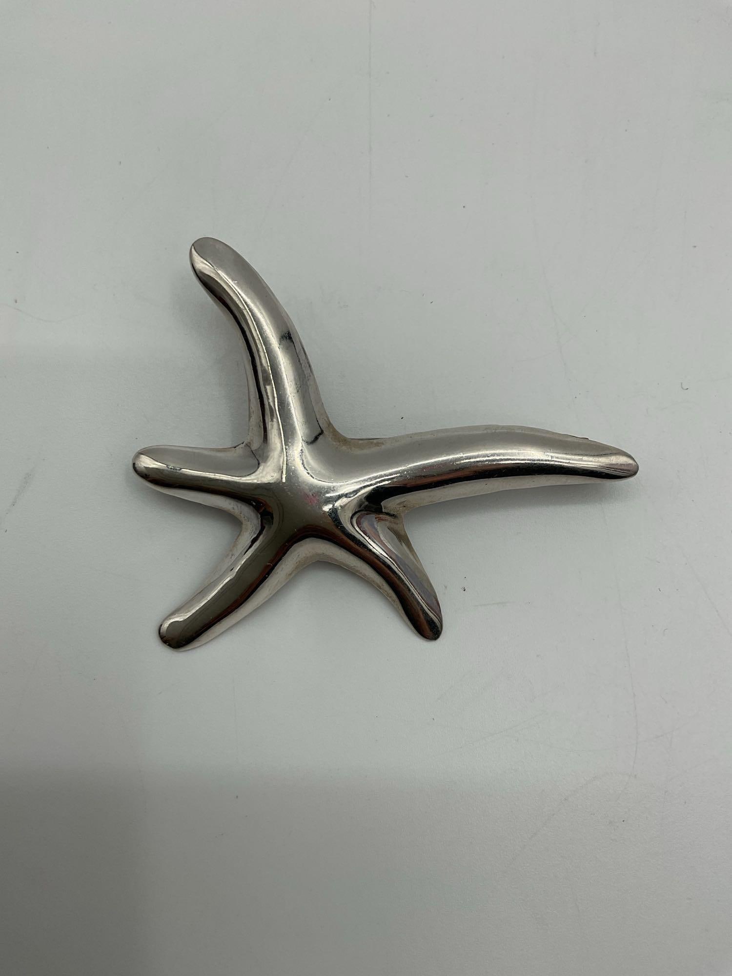 Modern Polished Silver Starfish Brooch: Sleek and contemporary brooch designed in the shape of a starfish with a smooth, polished silver-tone finish. Likely crafted from base metal or pewter, this minimalist piece captures coastal charm and